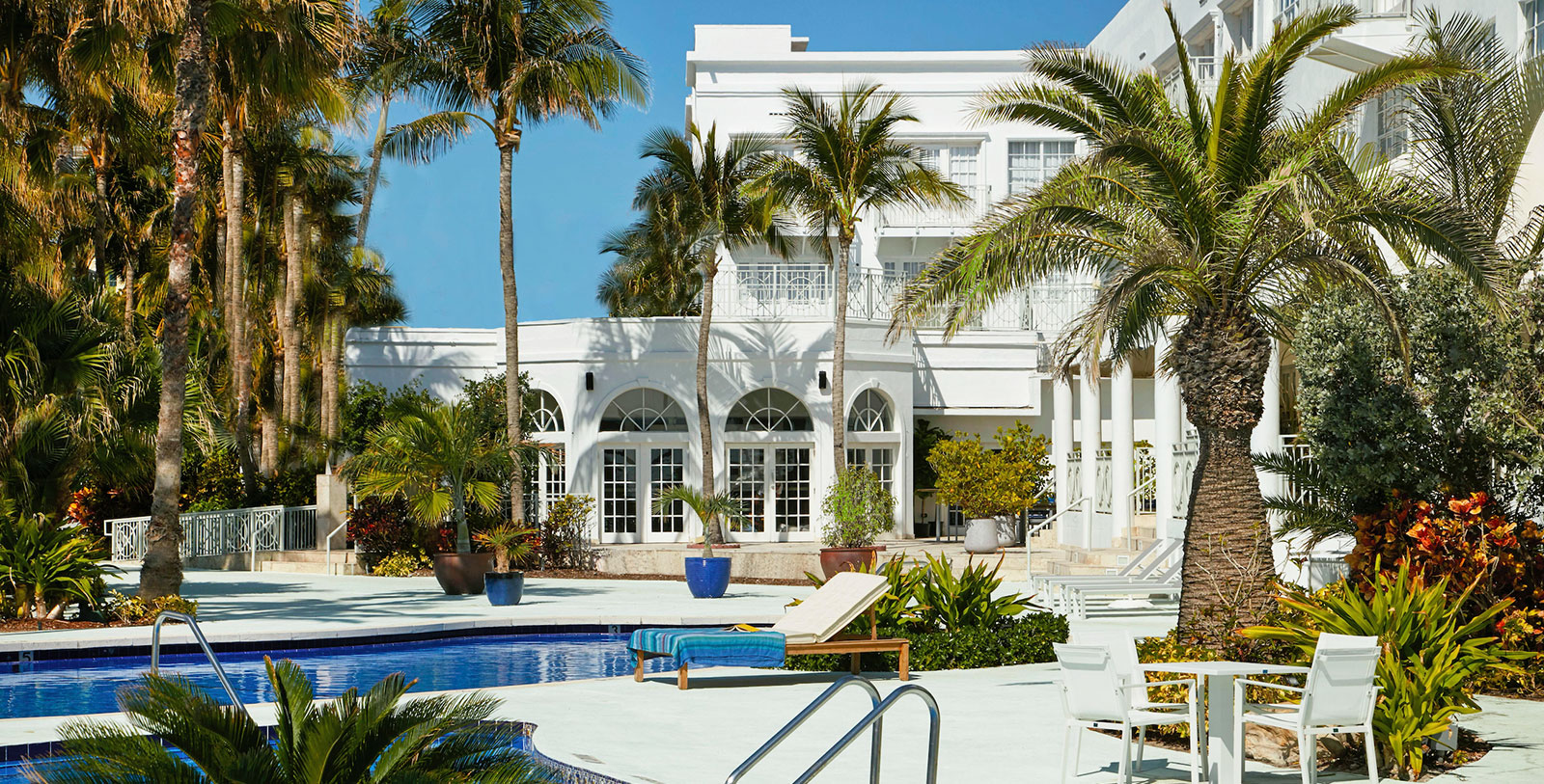 a pool with palm trees and chairs in front of a building
