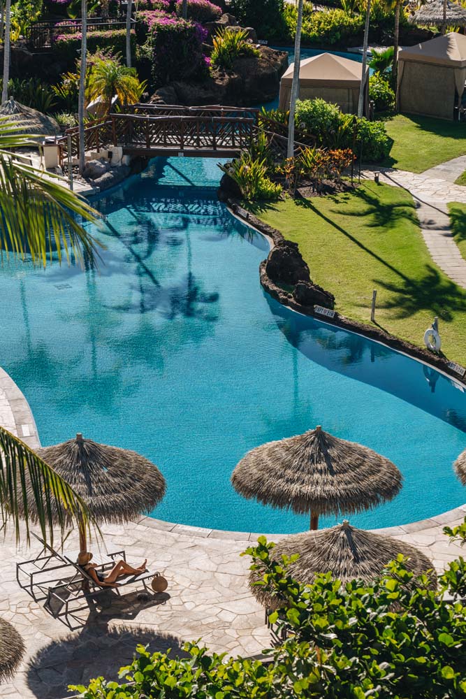 a pool with grass umbrellas and a bridge