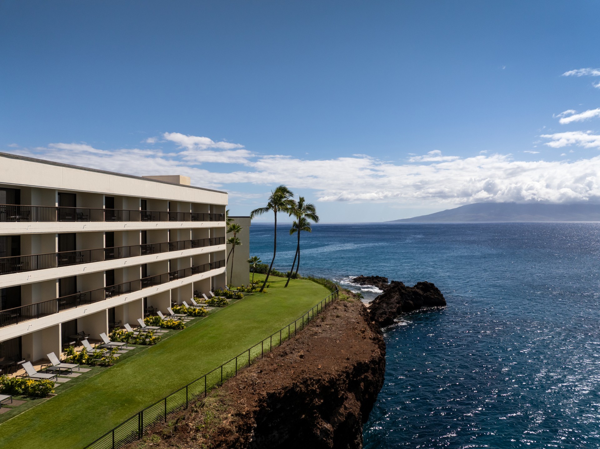 a building with grass and chairs on a cliff overlooking the ocean
