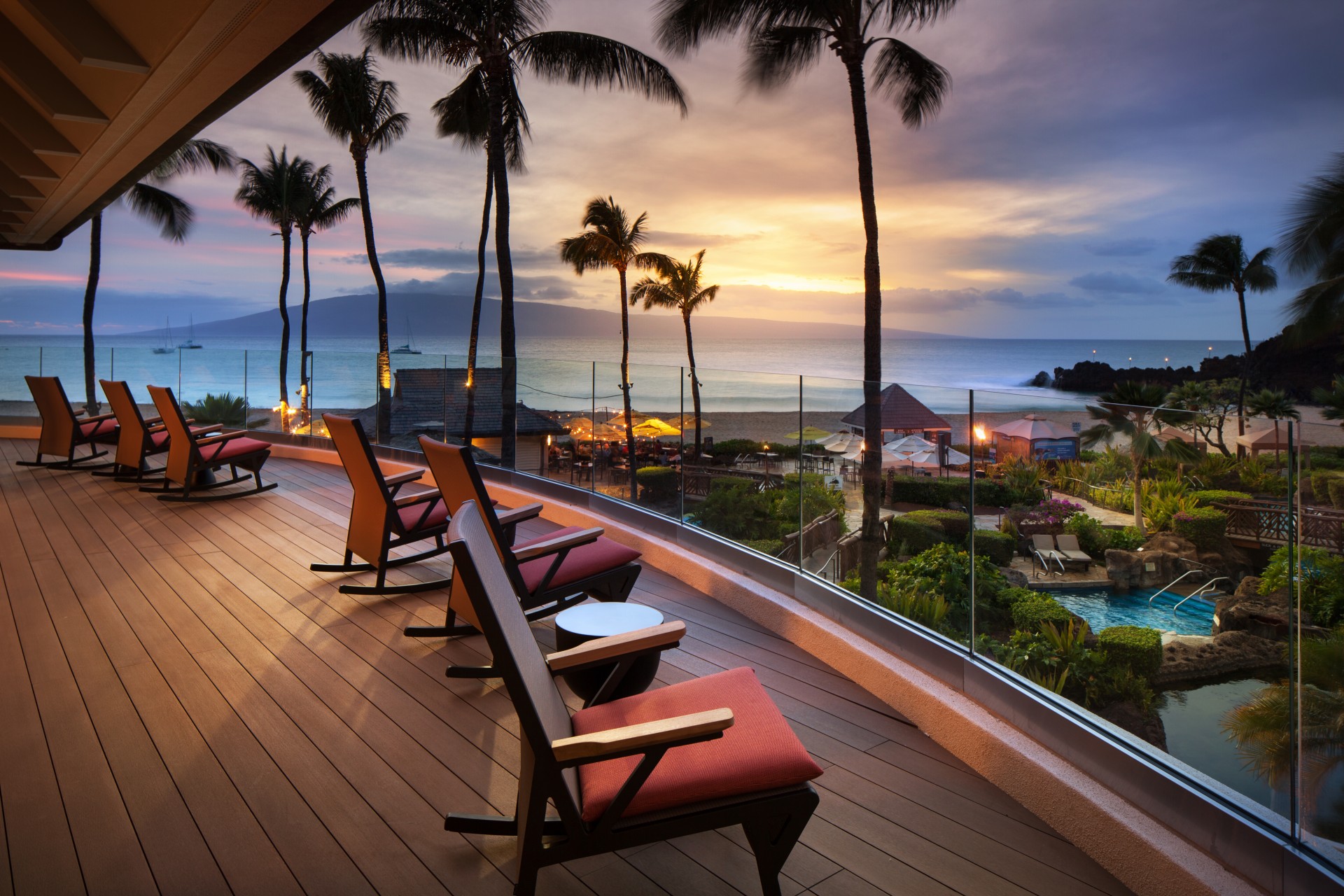 a deck with chairs and palm trees overlooking the ocean