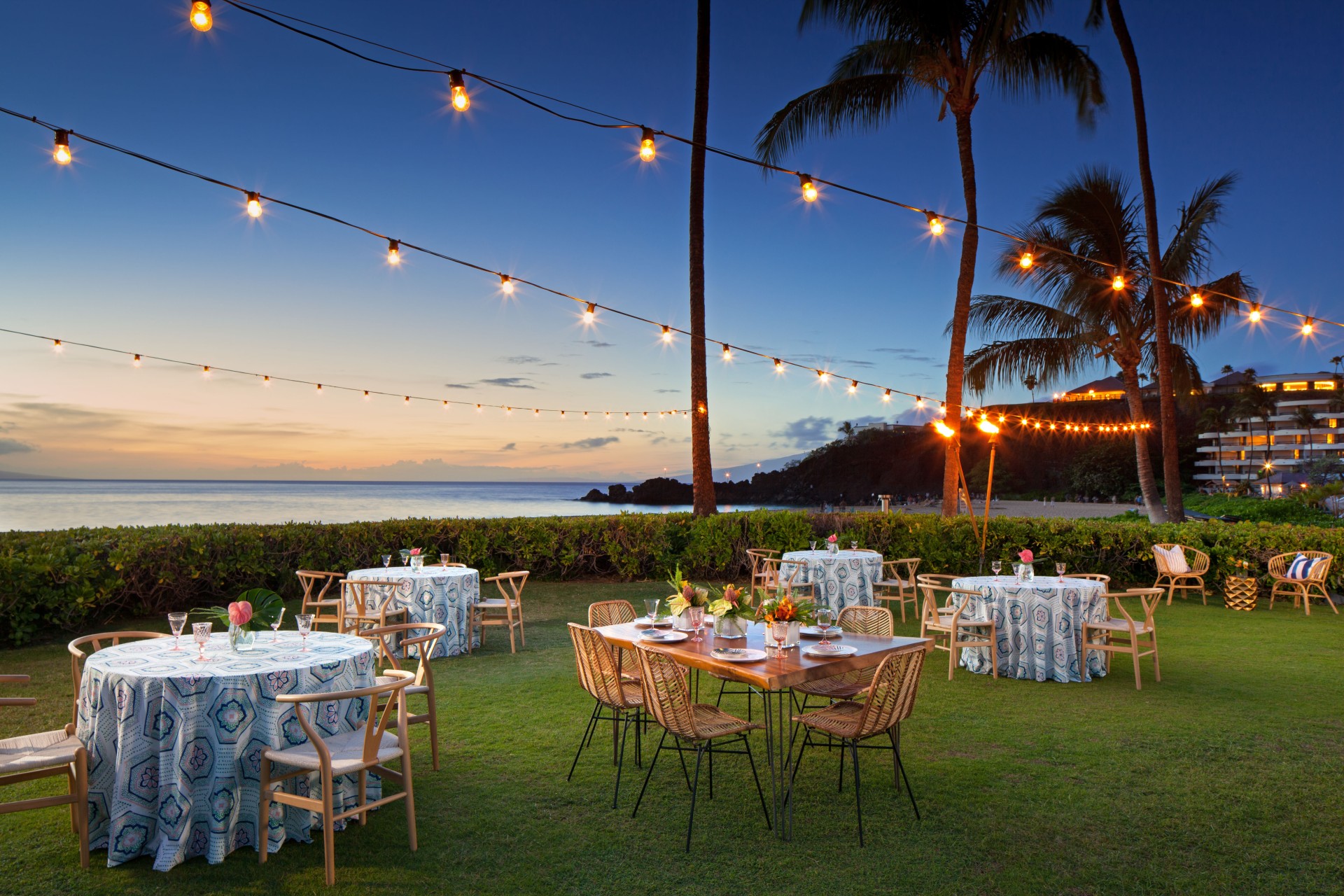 a group of tables and chairs in a grassy area with string lights