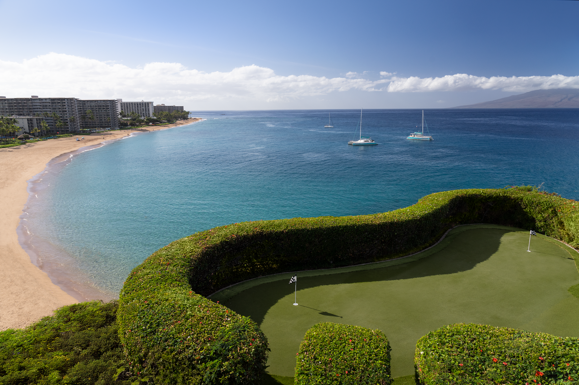 a golf course with a green lawn and a body of water with boats in the background