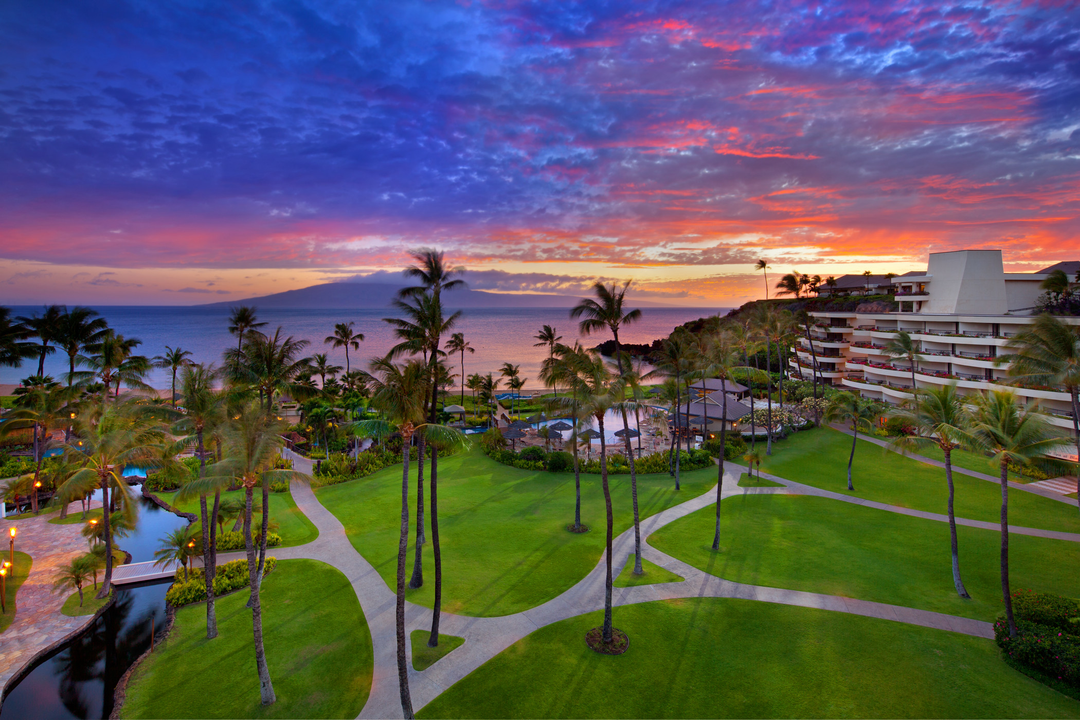 a tropical resort with a body of water and a sunset