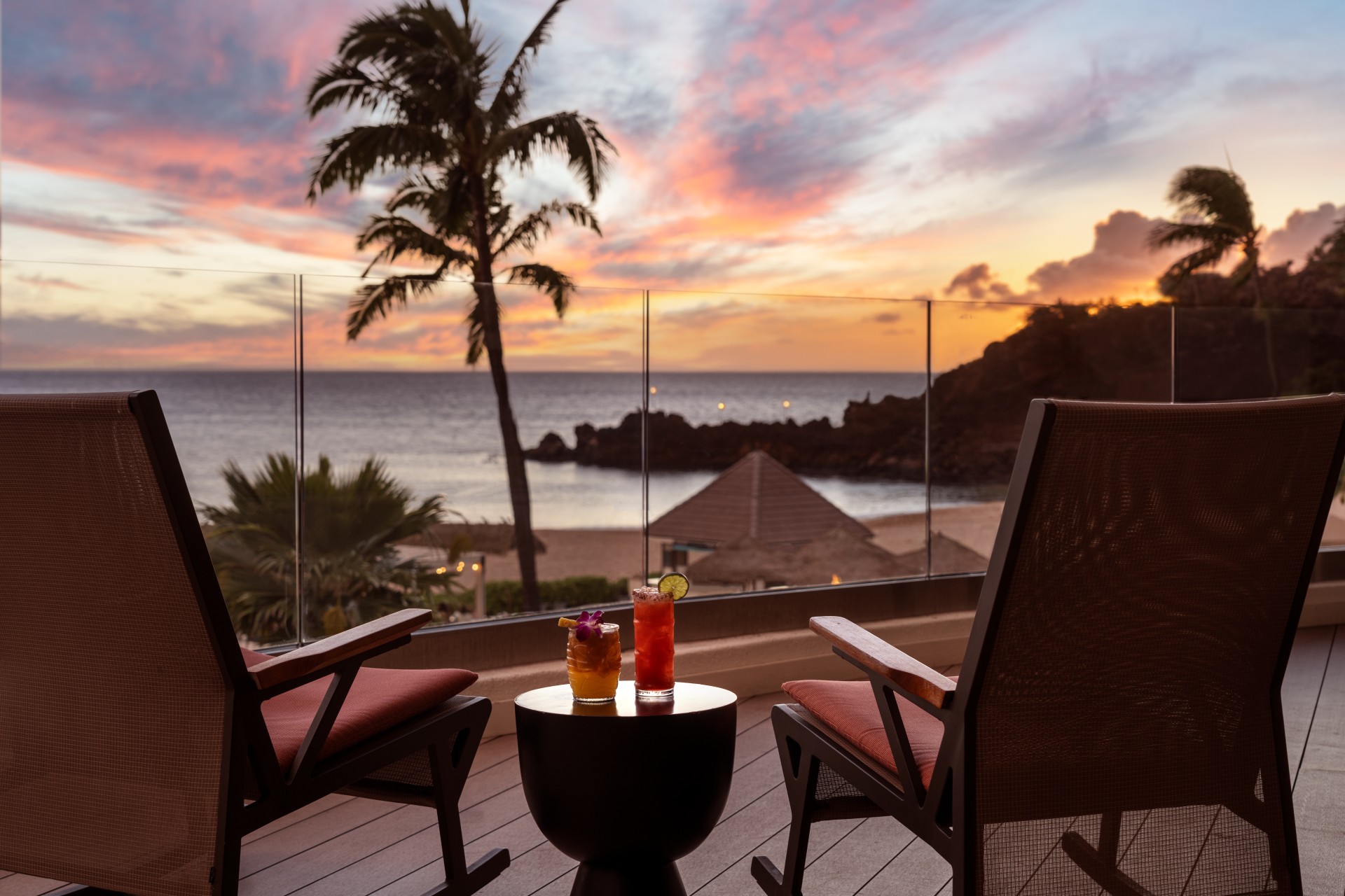 a table with drinks on it and chairs on a deck with a sunset in the background
