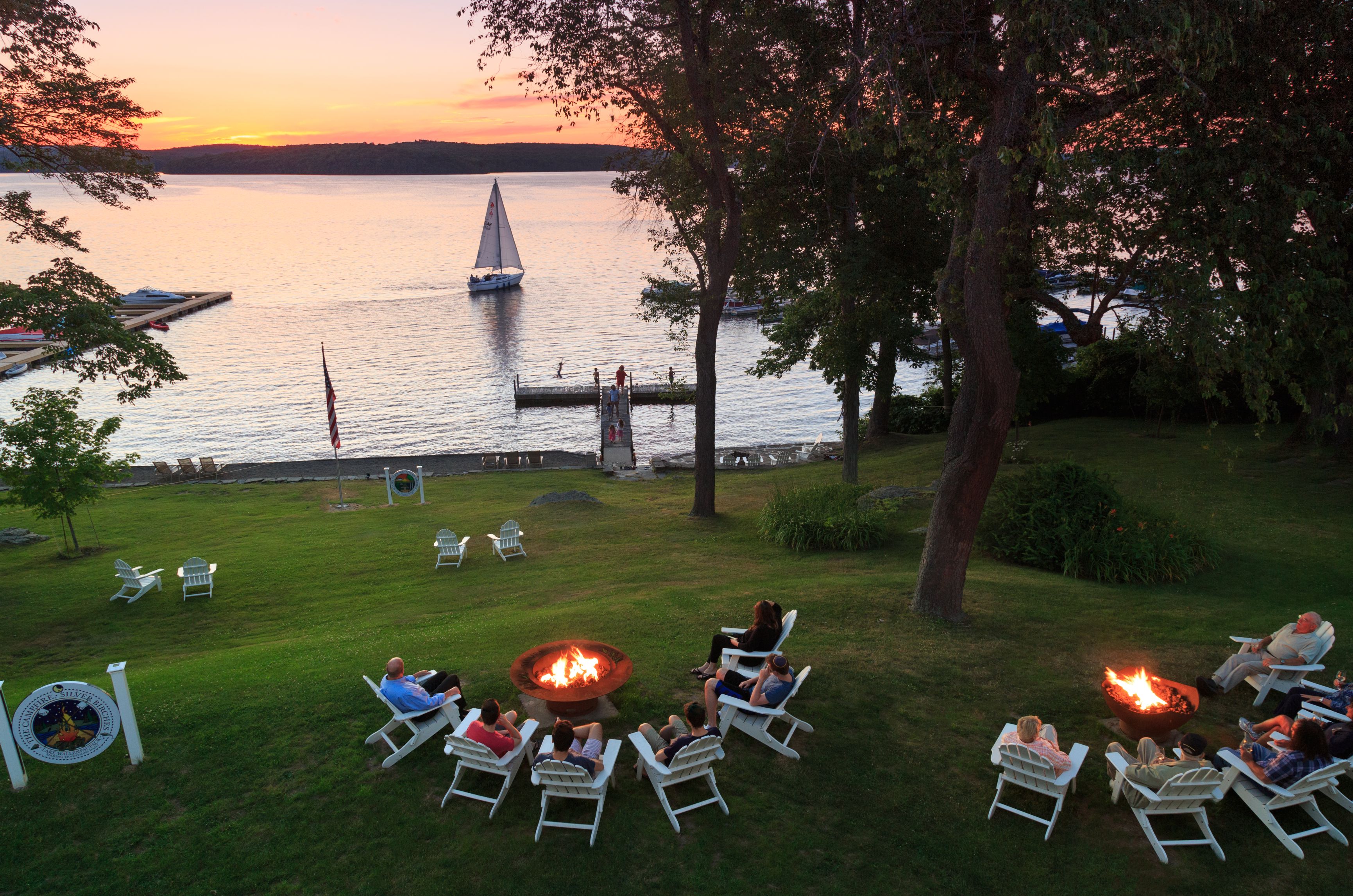 a group of people sitting in chairs around a fire pit by a lake