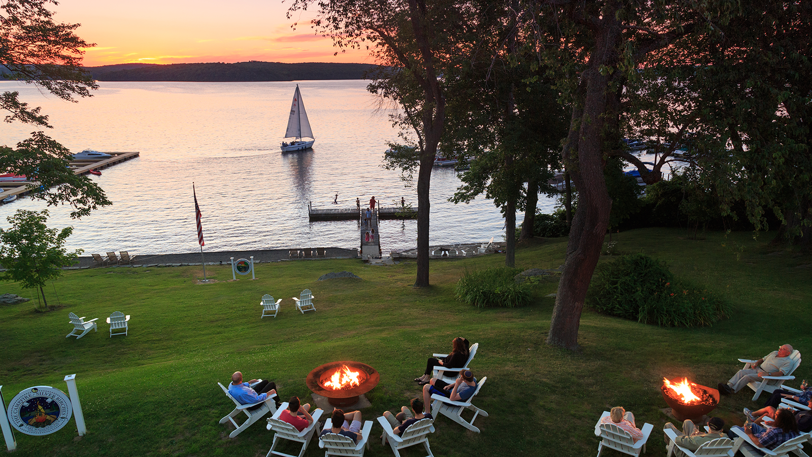 a group of people sitting in lawn chairs around a fire pit by a lake