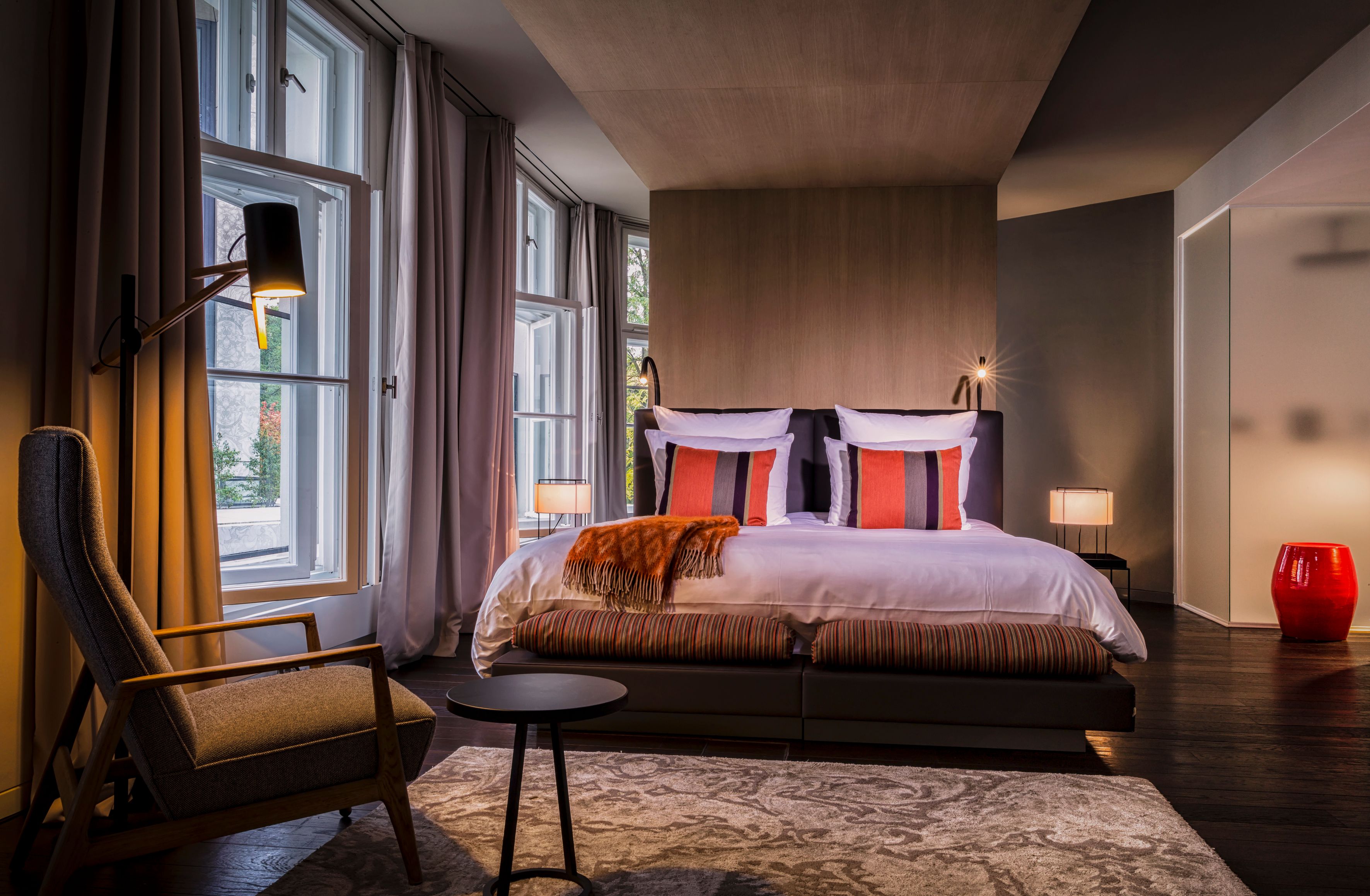 a bed with pillows and a chair in a room with windows