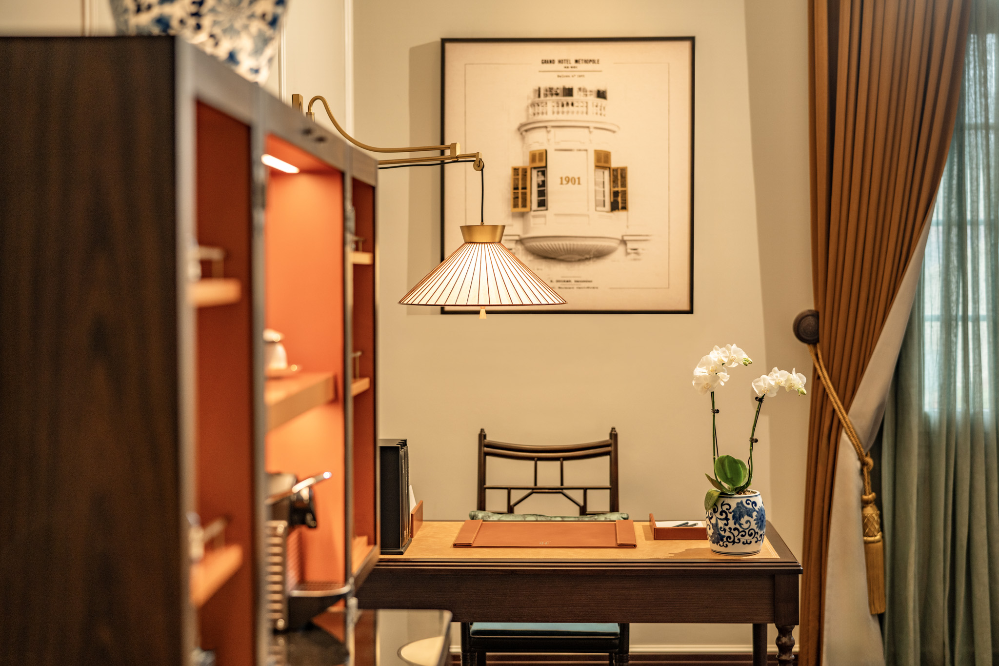 a desk with a lamp and a vase of flowers in front of a picture