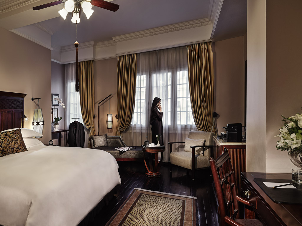 a woman standing in a room with a bed and a window
