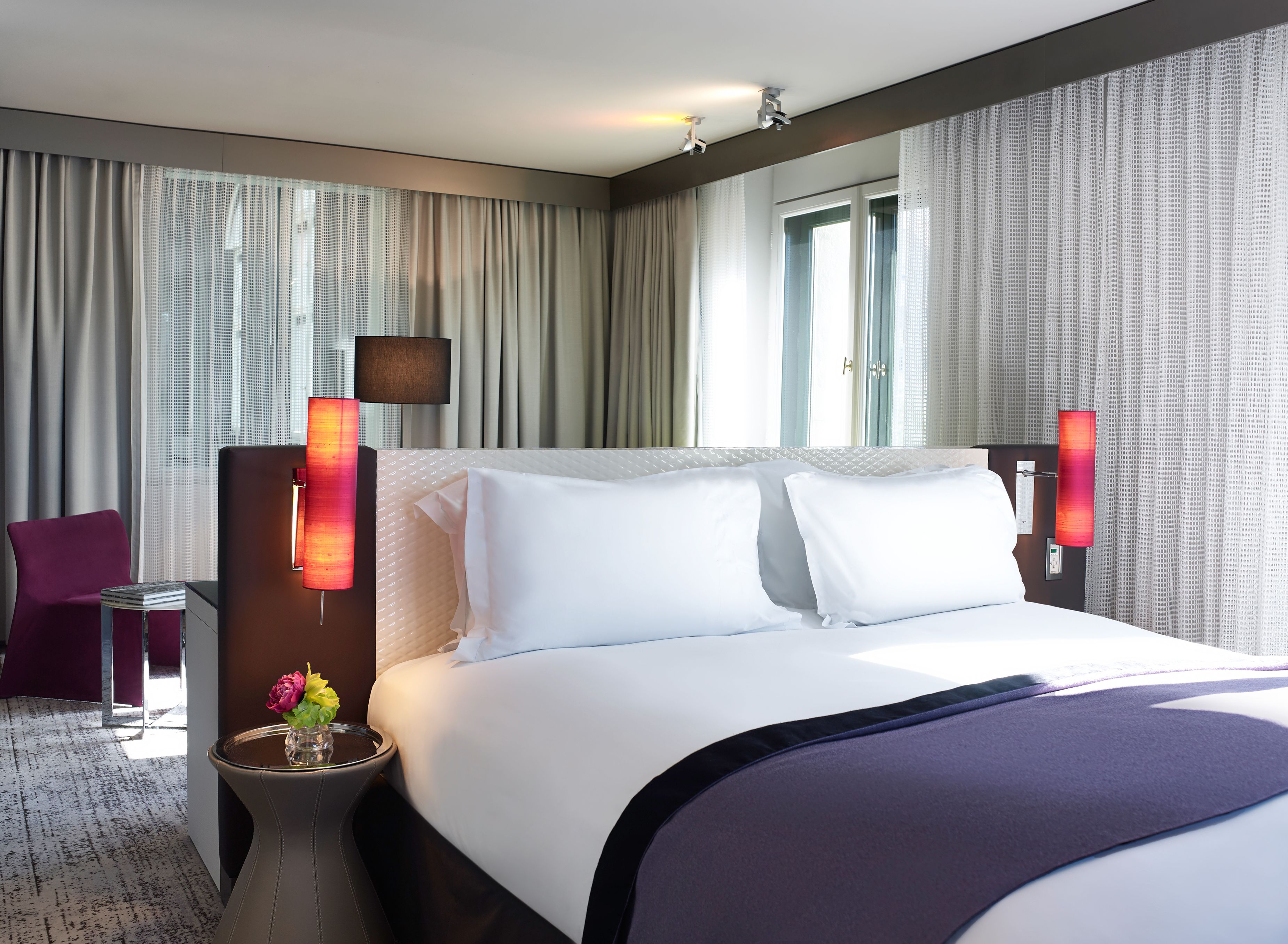 a bed with white pillows and purple blanket in a room with curtains