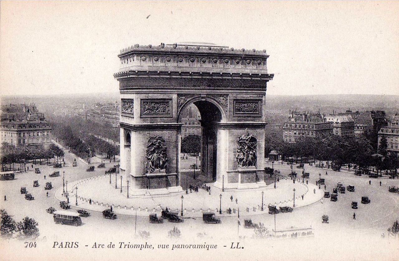 a large stone arch with statues on it with Arc de Triomphe in the background