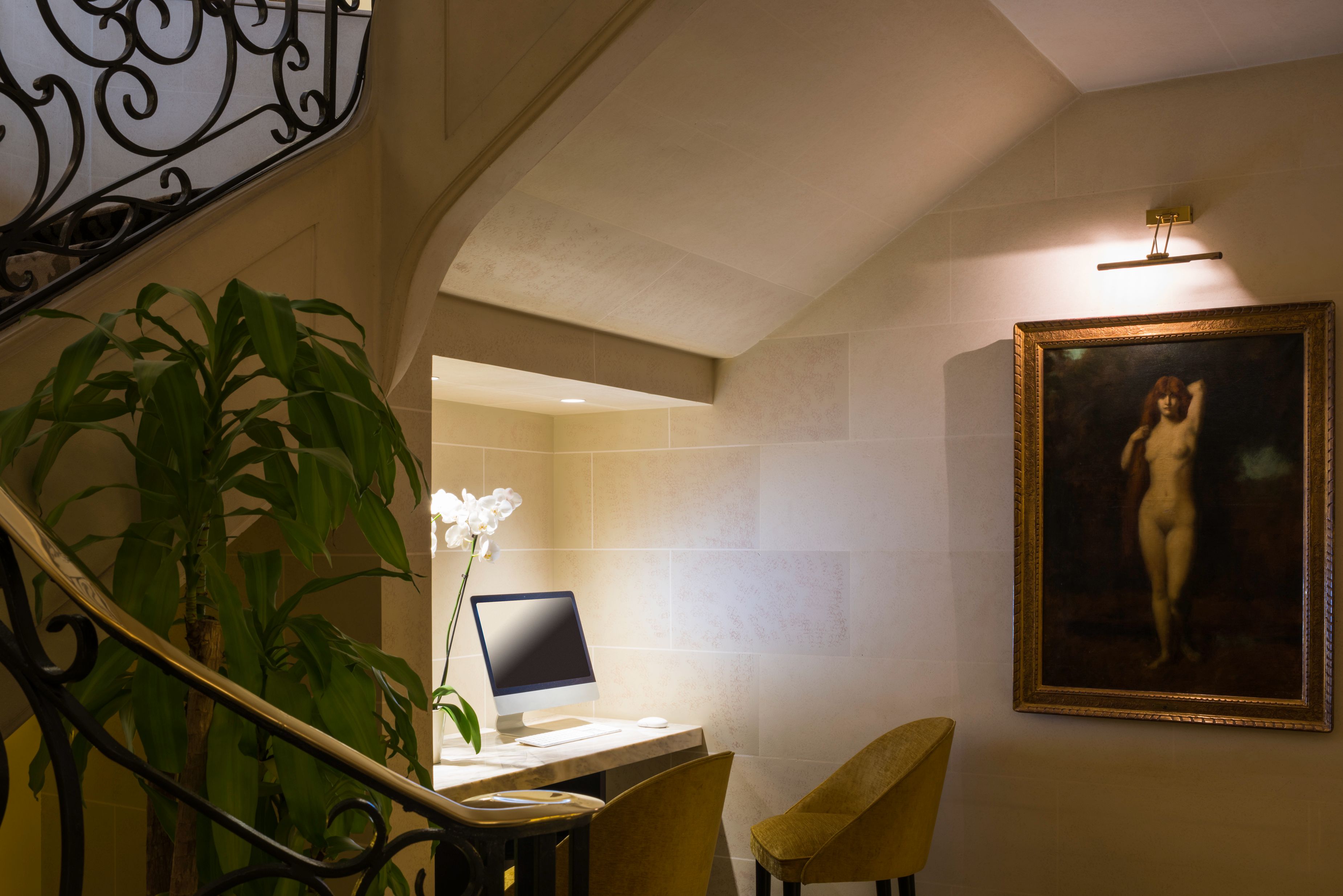 a computer on a desk in a room with a staircase and a plant