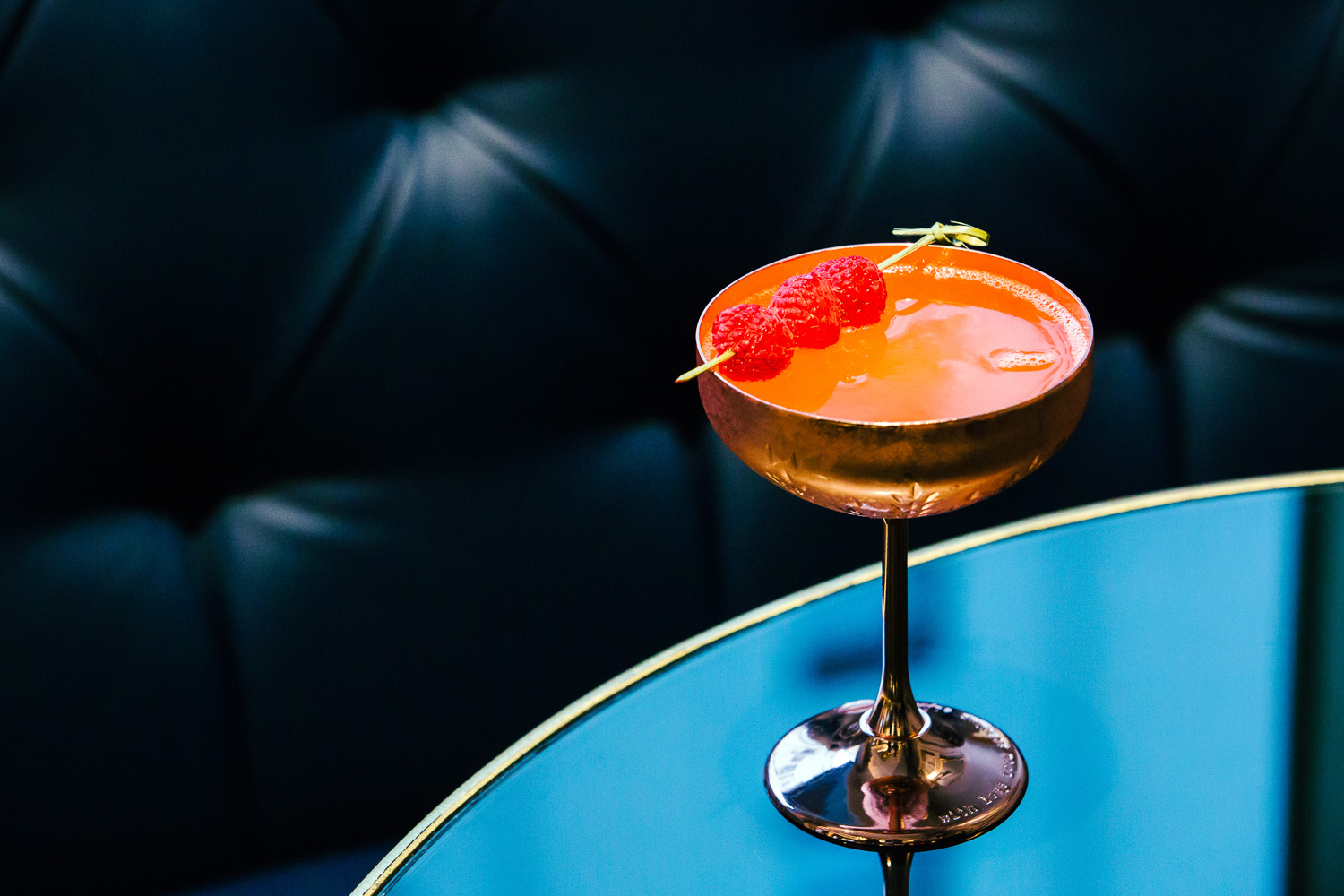 a glass with orange liquid and raspberries on a blue table