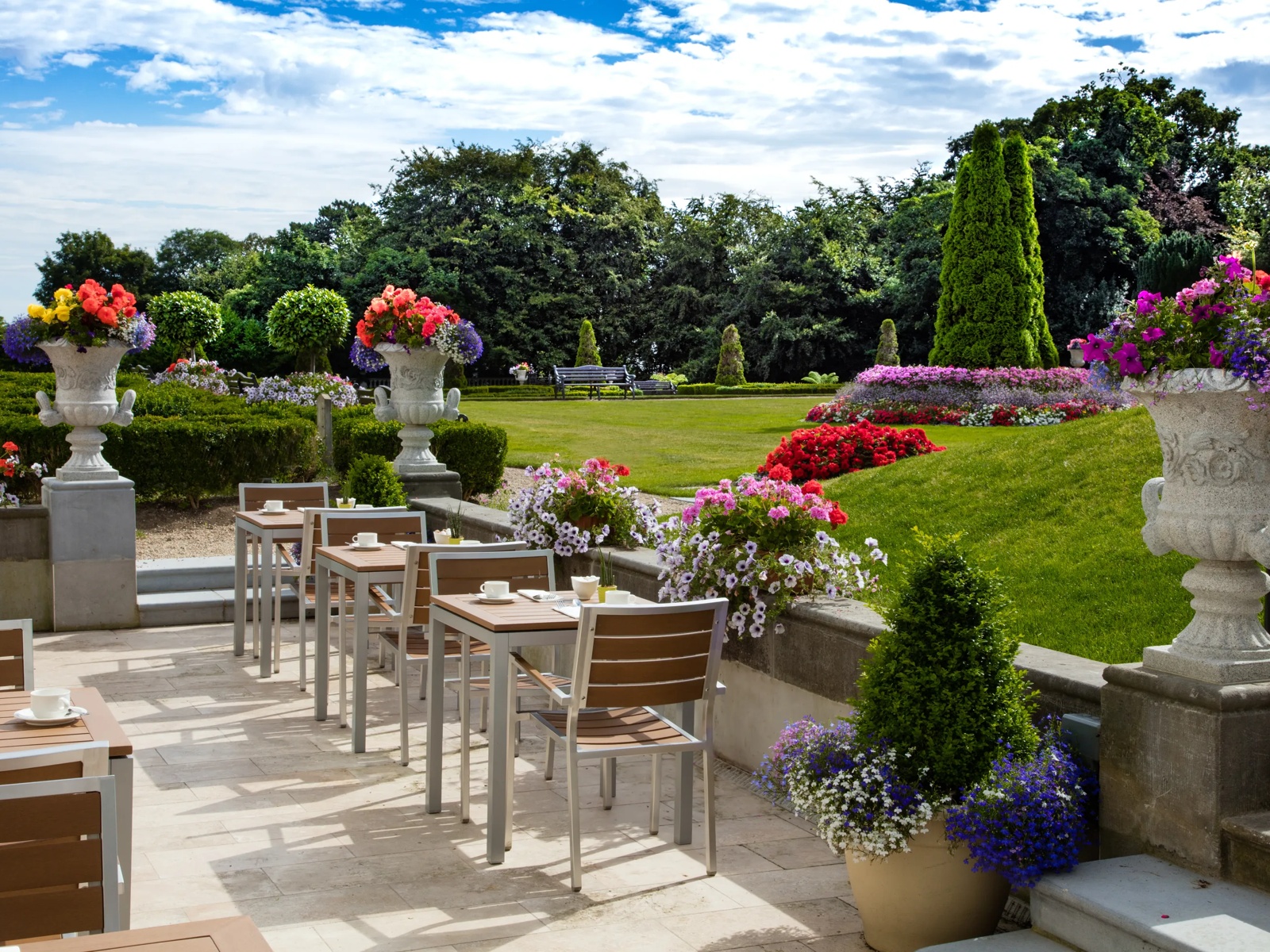 a table and chairs on a patio with flowers and trees in the background