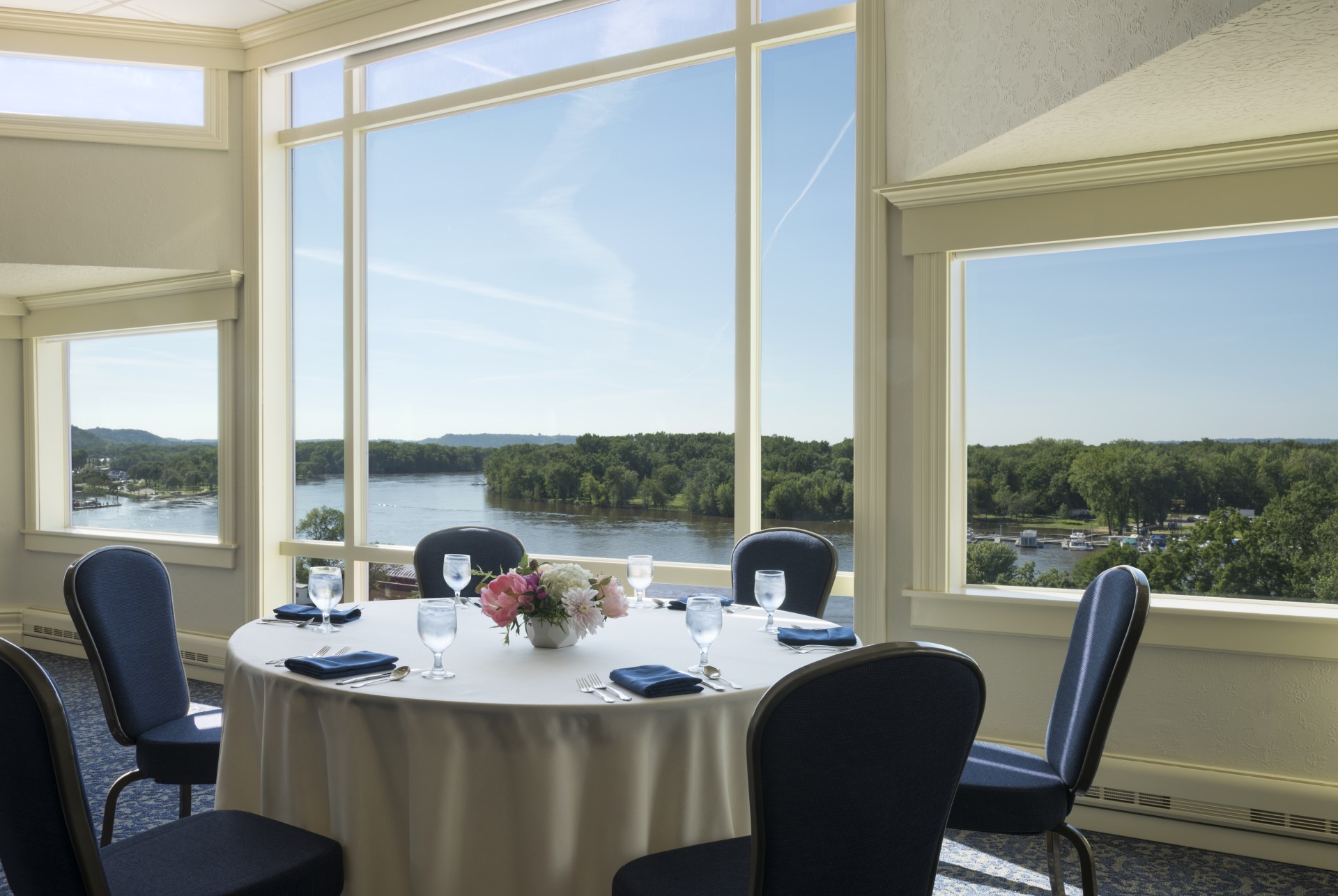 a table set up with a white tablecloth and chairs with a view of water and trees