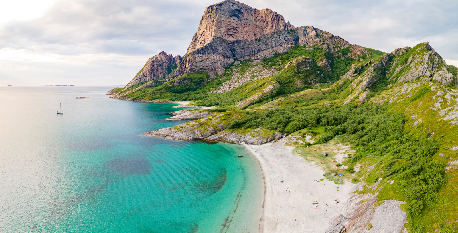 a beach with a rocky mountain and blue water