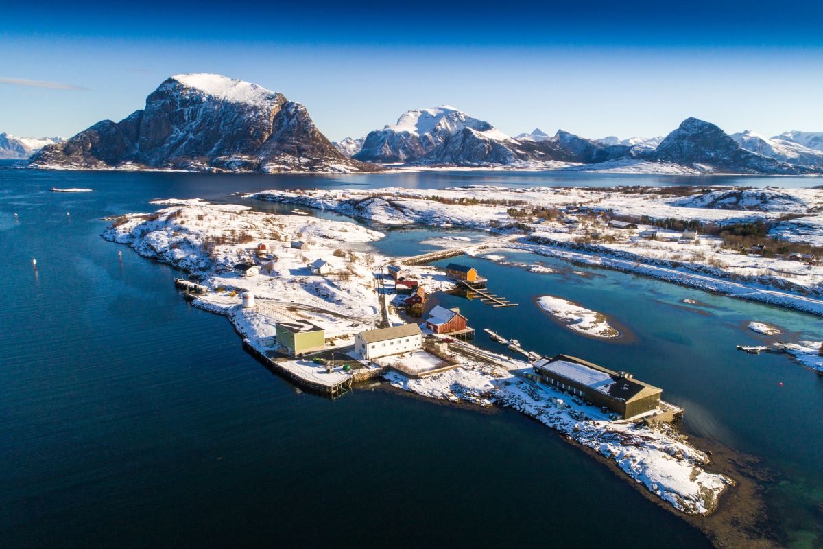 a small village on a small island surrounded by water with snow with Lofoten in the background