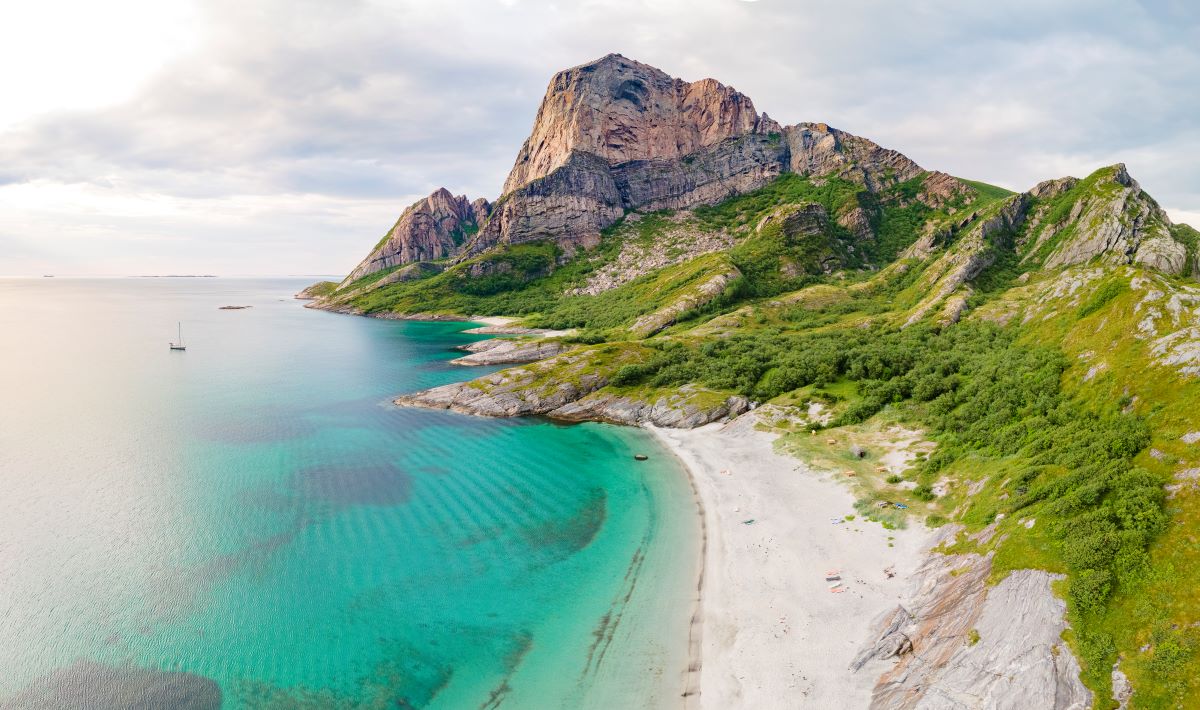 a beach with a rocky mountain and blue water