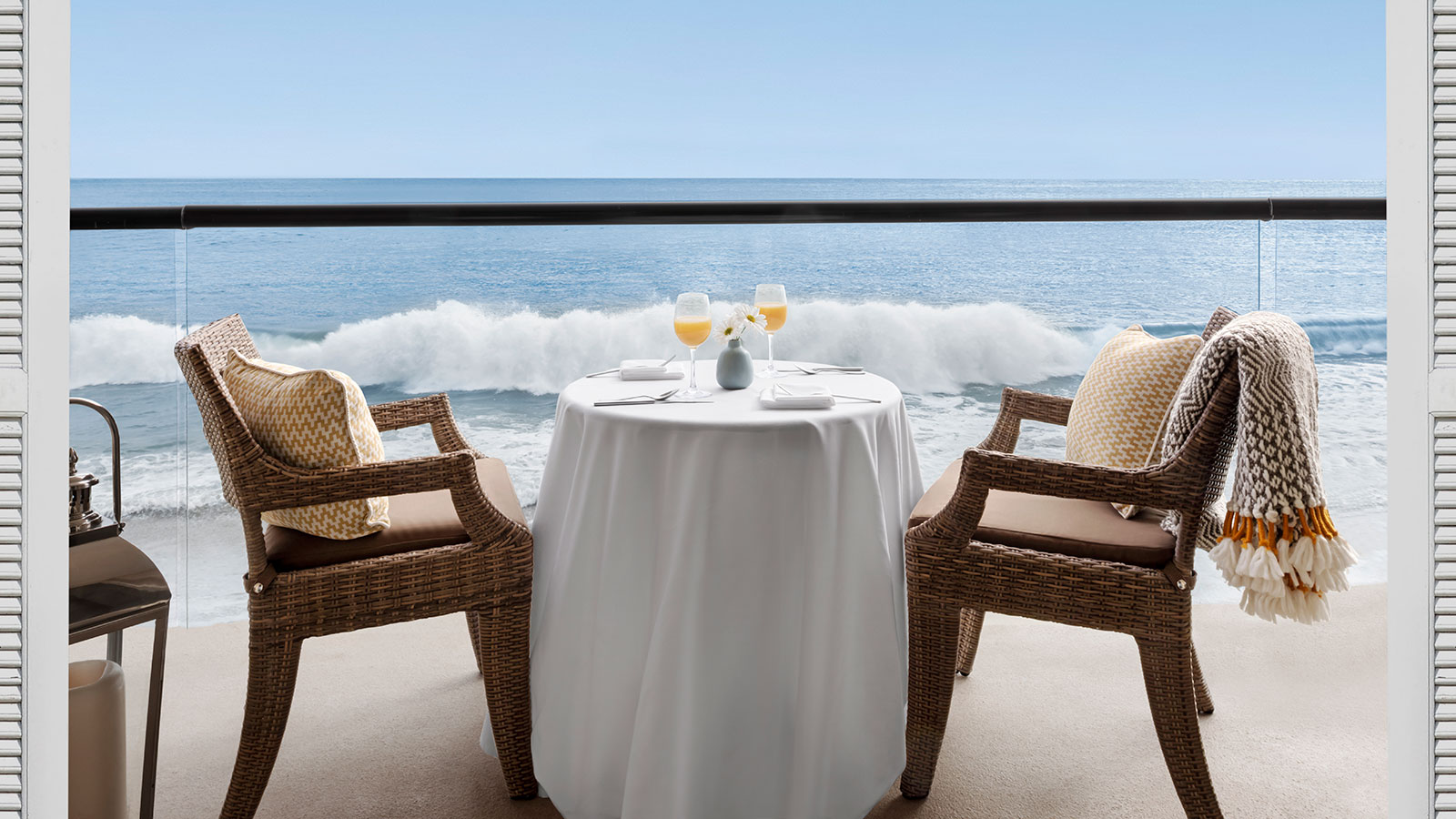 a table with two chairs and a glass of wine on a balcony overlooking the ocean