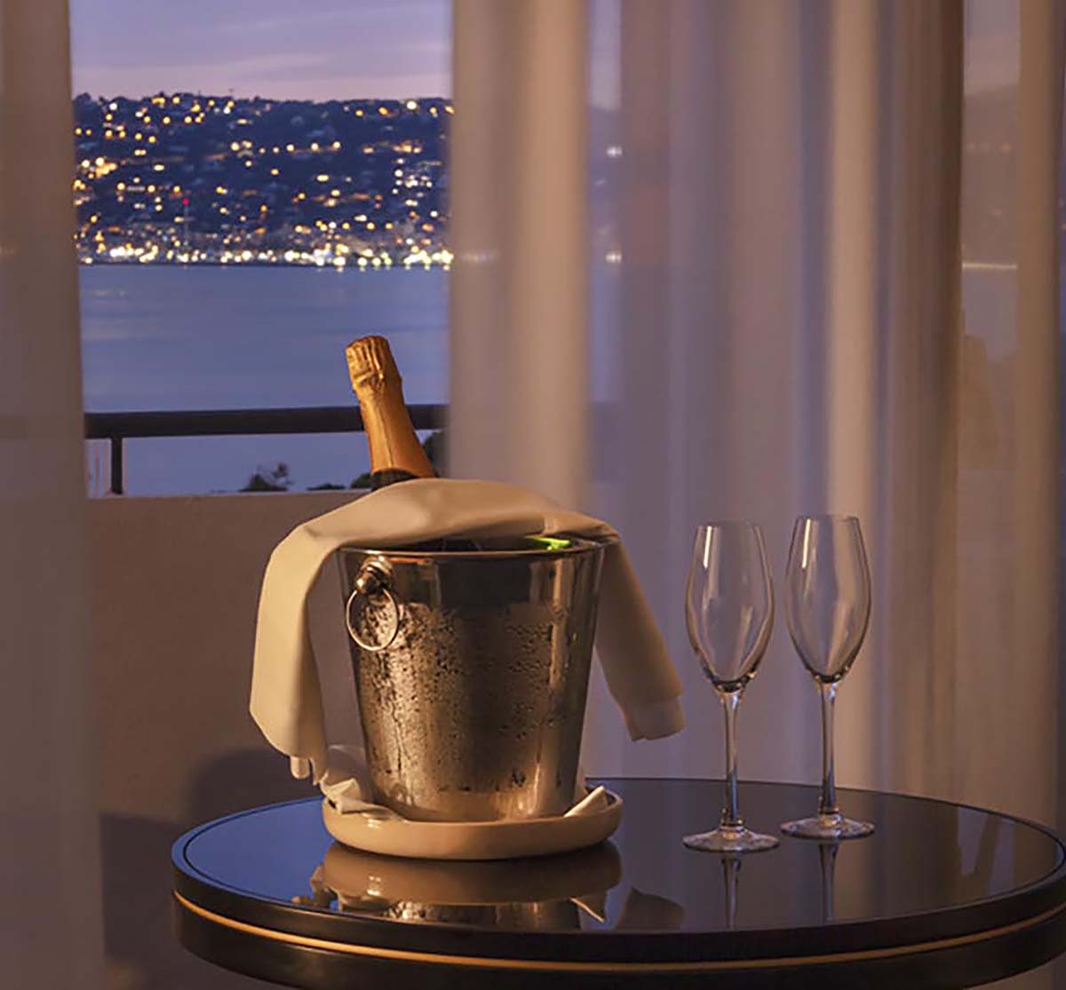 a champagne bottle in a bucket on a table with two wine glasses