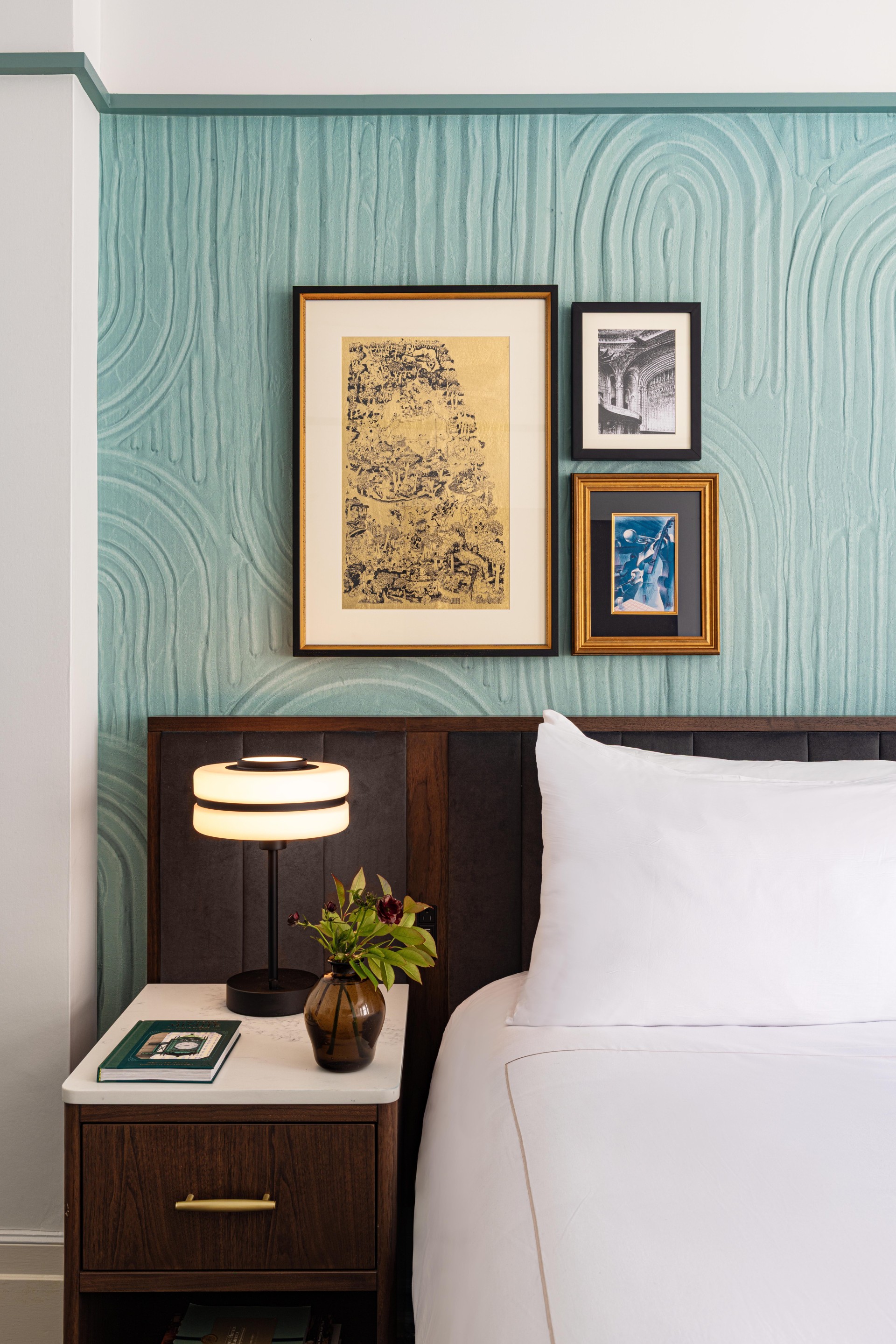 a bed with a lamp and picture frames on the wall