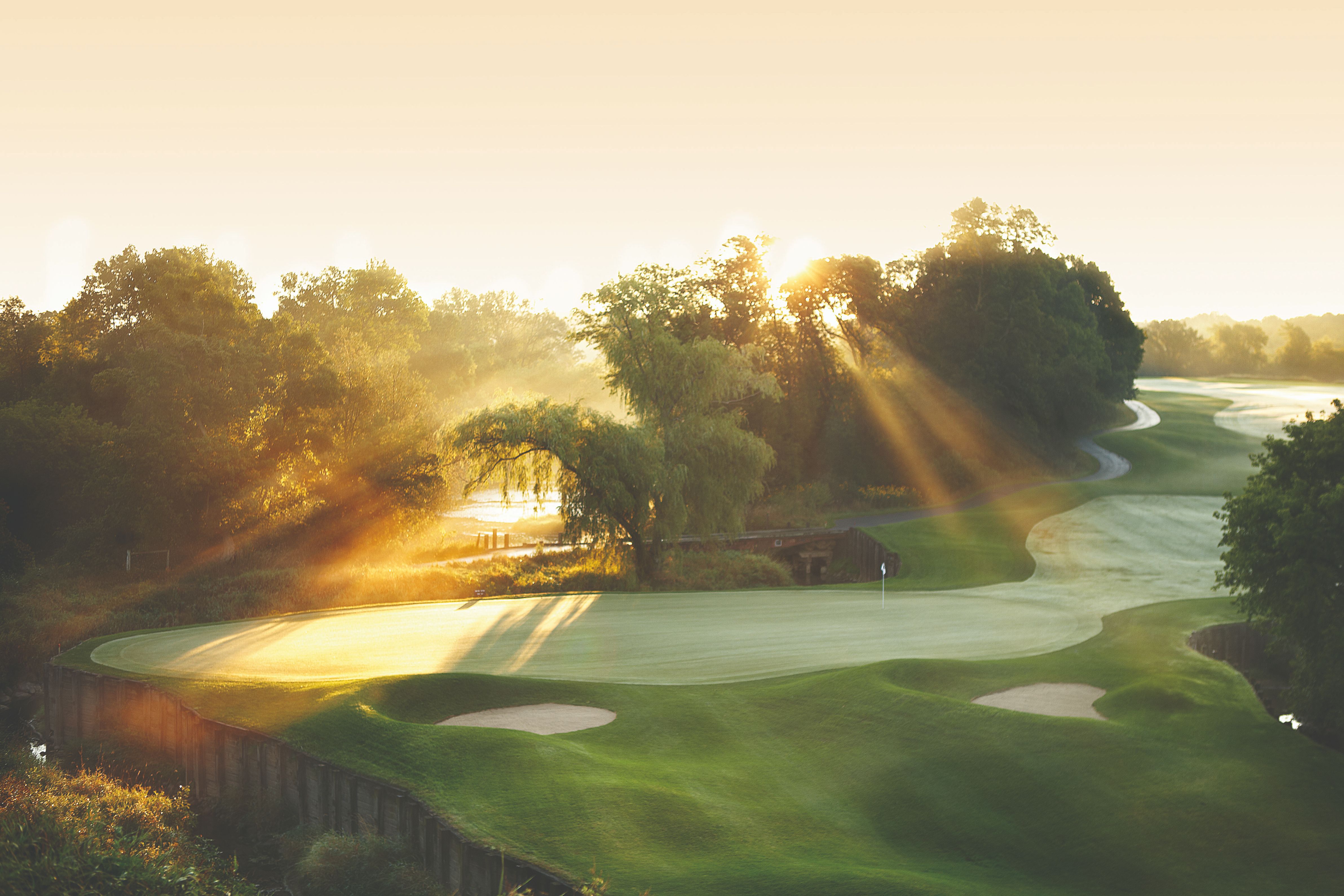 a golf course with trees and sun rays