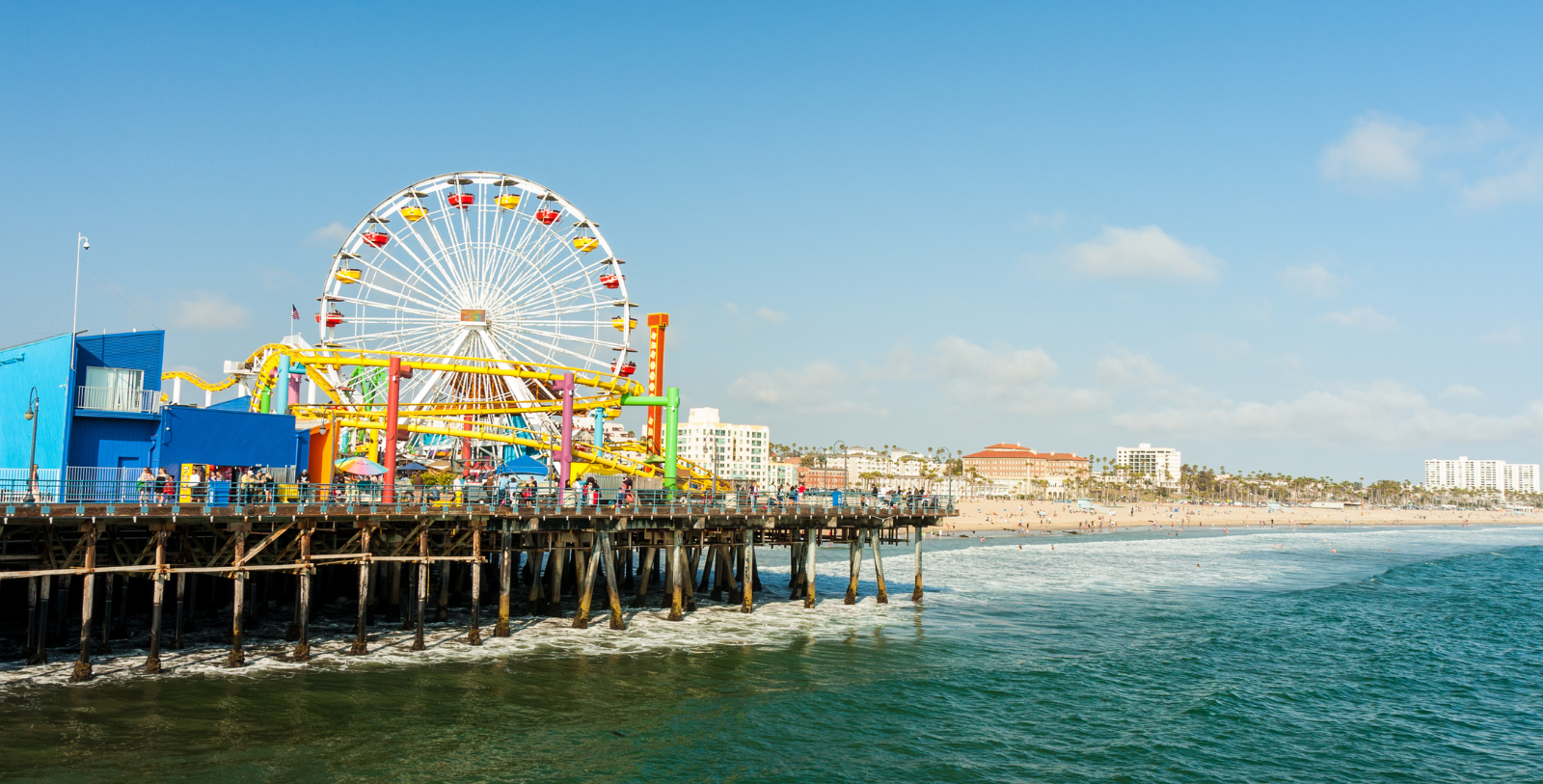 a pier with a ferris wheel and people on it with Santa Monica Pier in the background