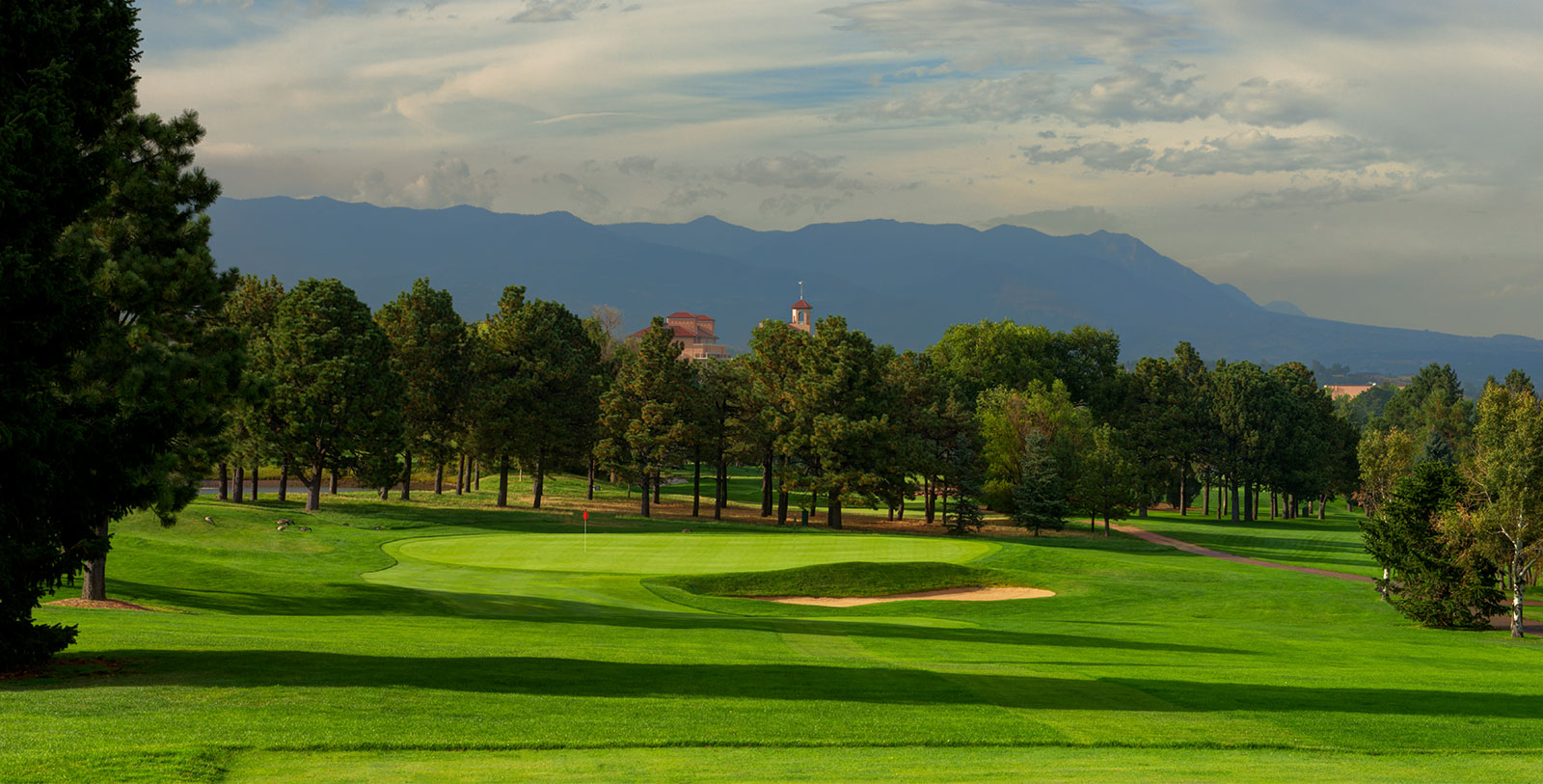 a golf course with trees and mountains in the background
