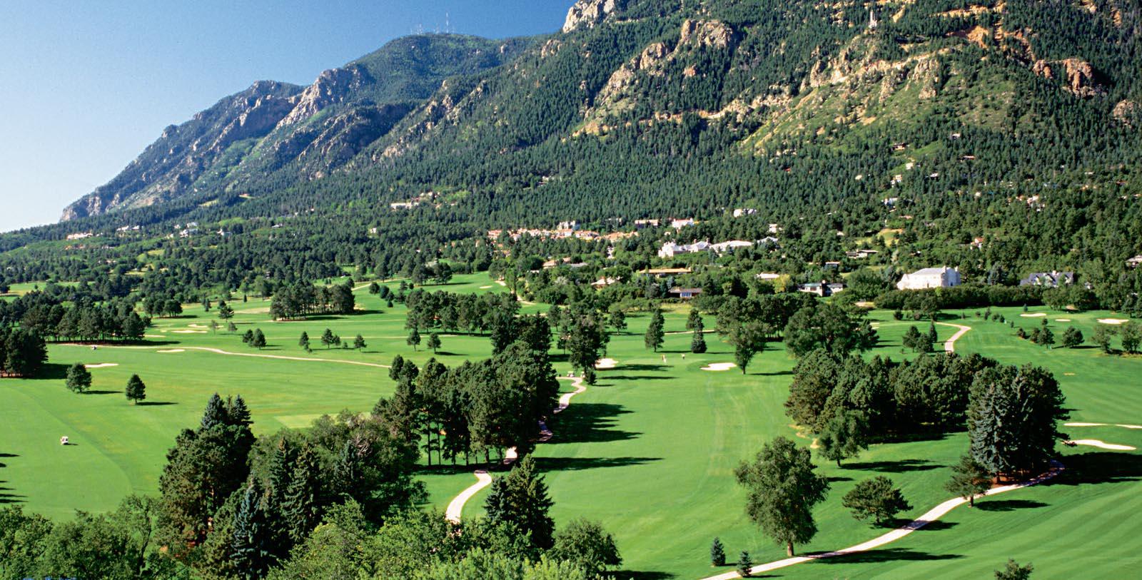 a golf course with trees and mountains in the background