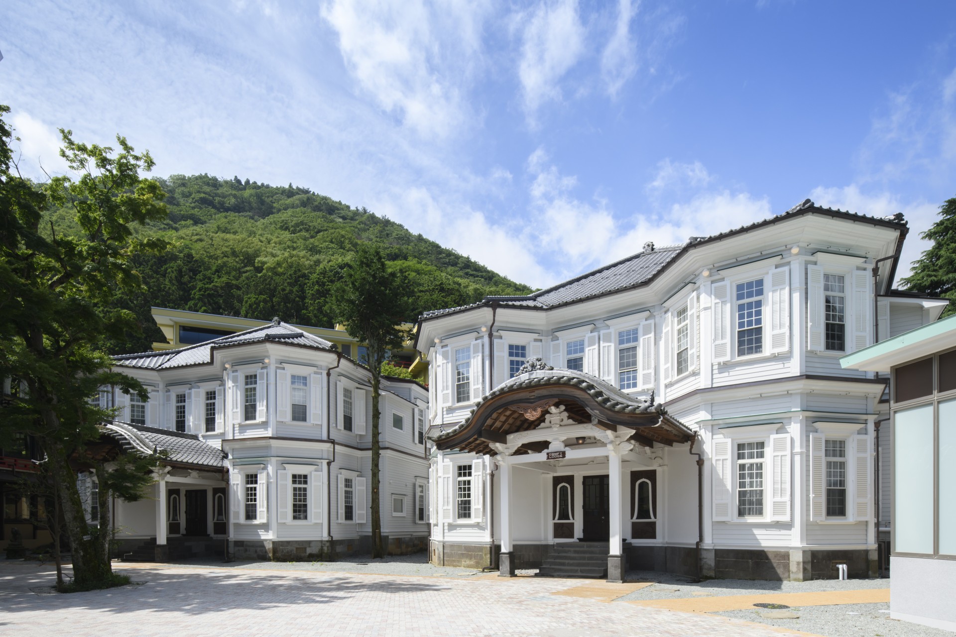 a large white building with a roof and a hill in the background
