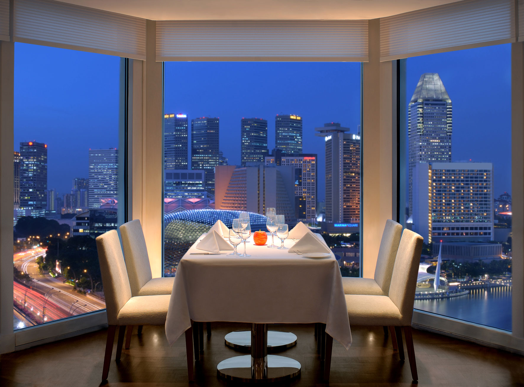 a table with white cloth and chairs in a room with a city view