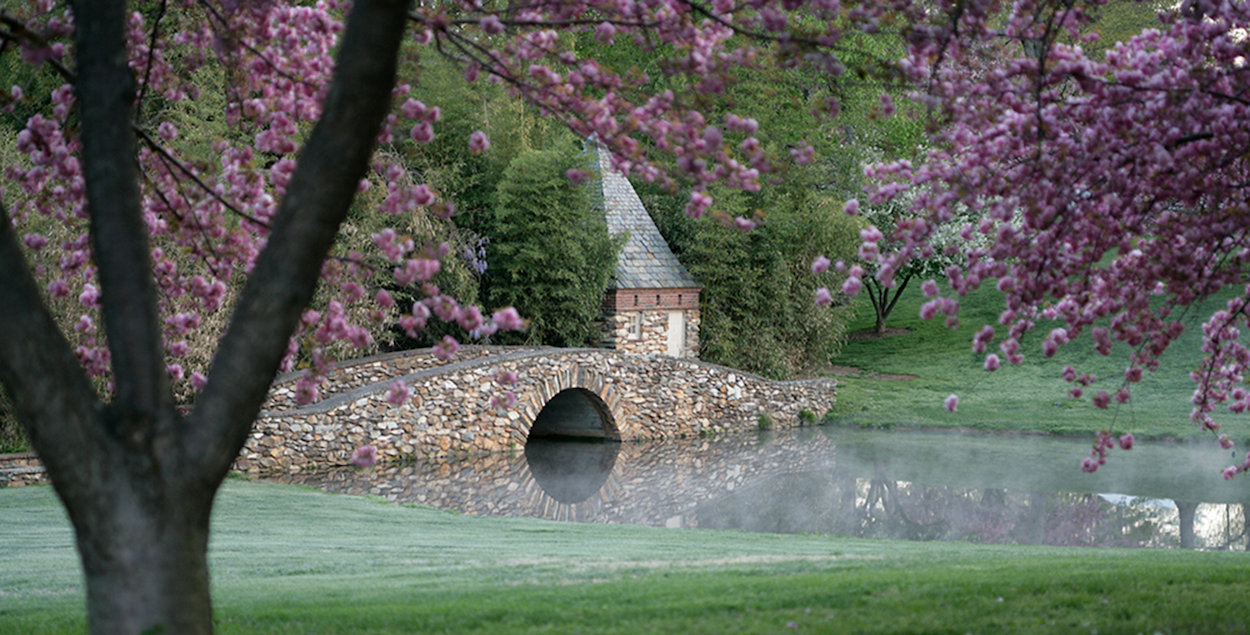 a bridge over a pond with a small building and trees