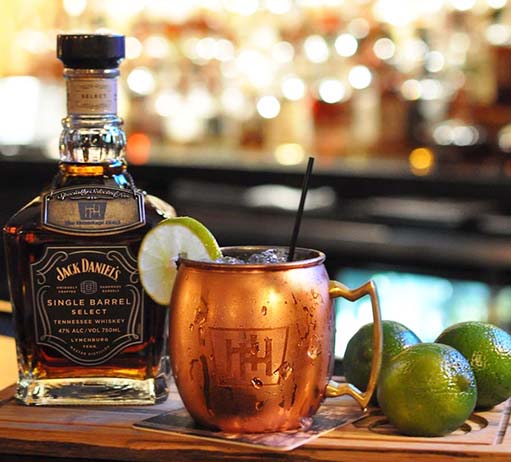 a bottle of alcohol next to a copper mug and limes