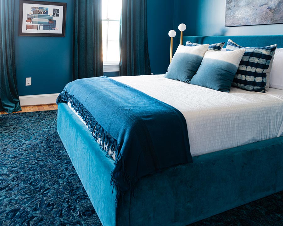 a bed with blue curtains and a painting on the wall