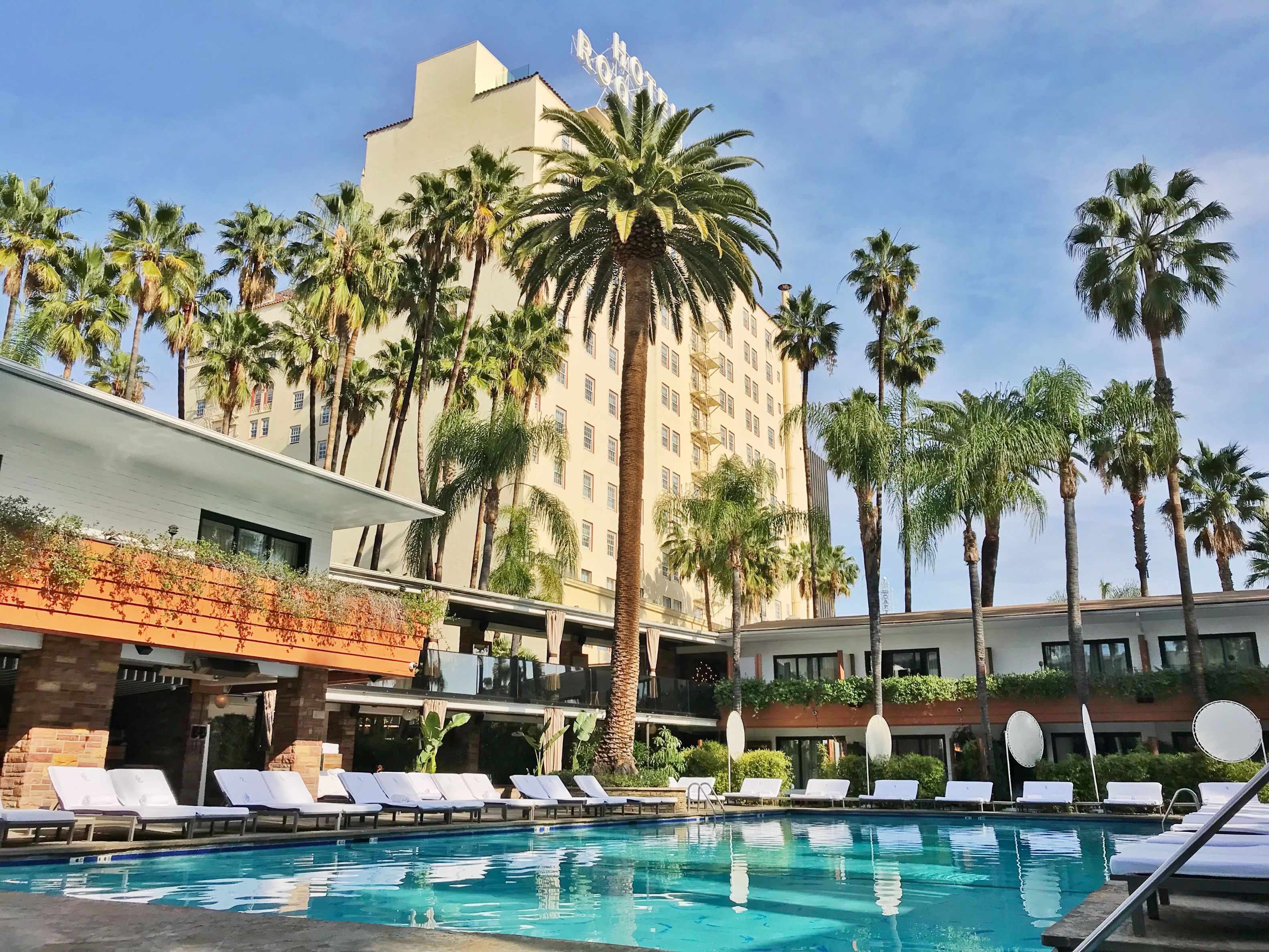 a pool with lounge chairs and palm trees in front of a building