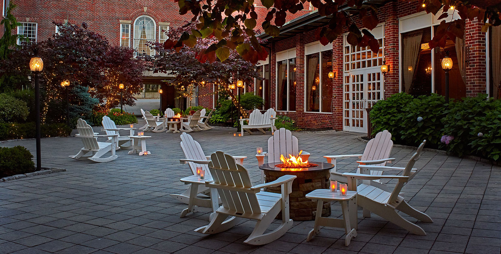 a fire pit with chairs and candles in front of a brick building
