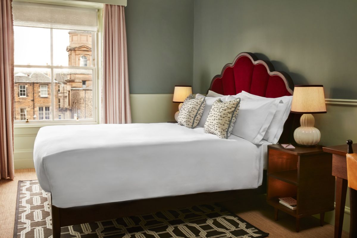 a bed with a red headboard and a lamp next to a window