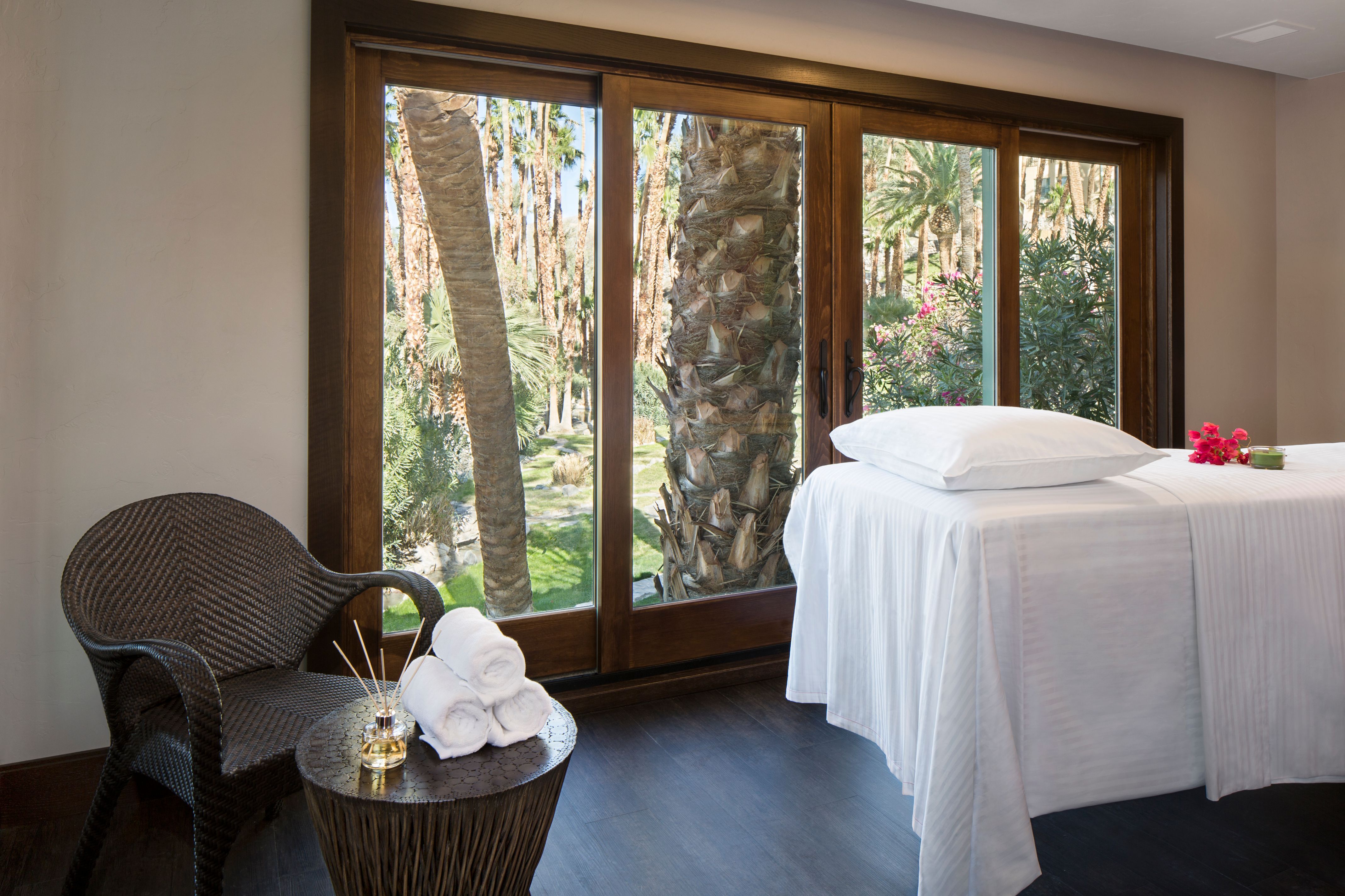 a room with a bed and chairs and a chair with a view of the trees outside