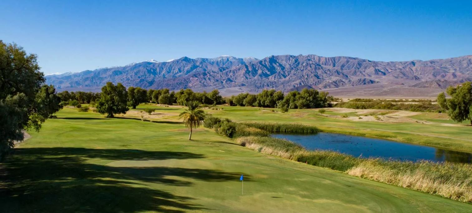 a golf course with a lake and mountains in the background
