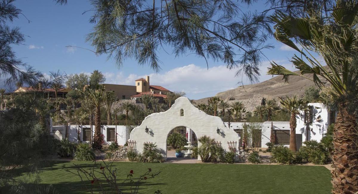 a white archway with a fountain in front of a green lawn