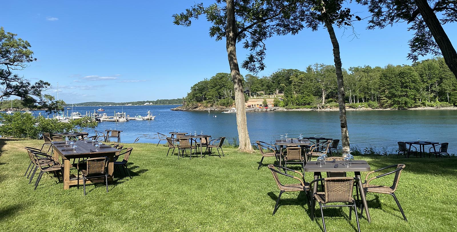 a group of tables and chairs on grass next to a body of water