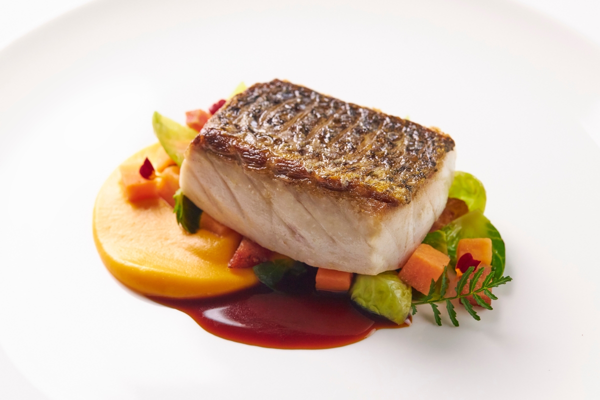 a piece of fish with vegetables and sauce on a white plate