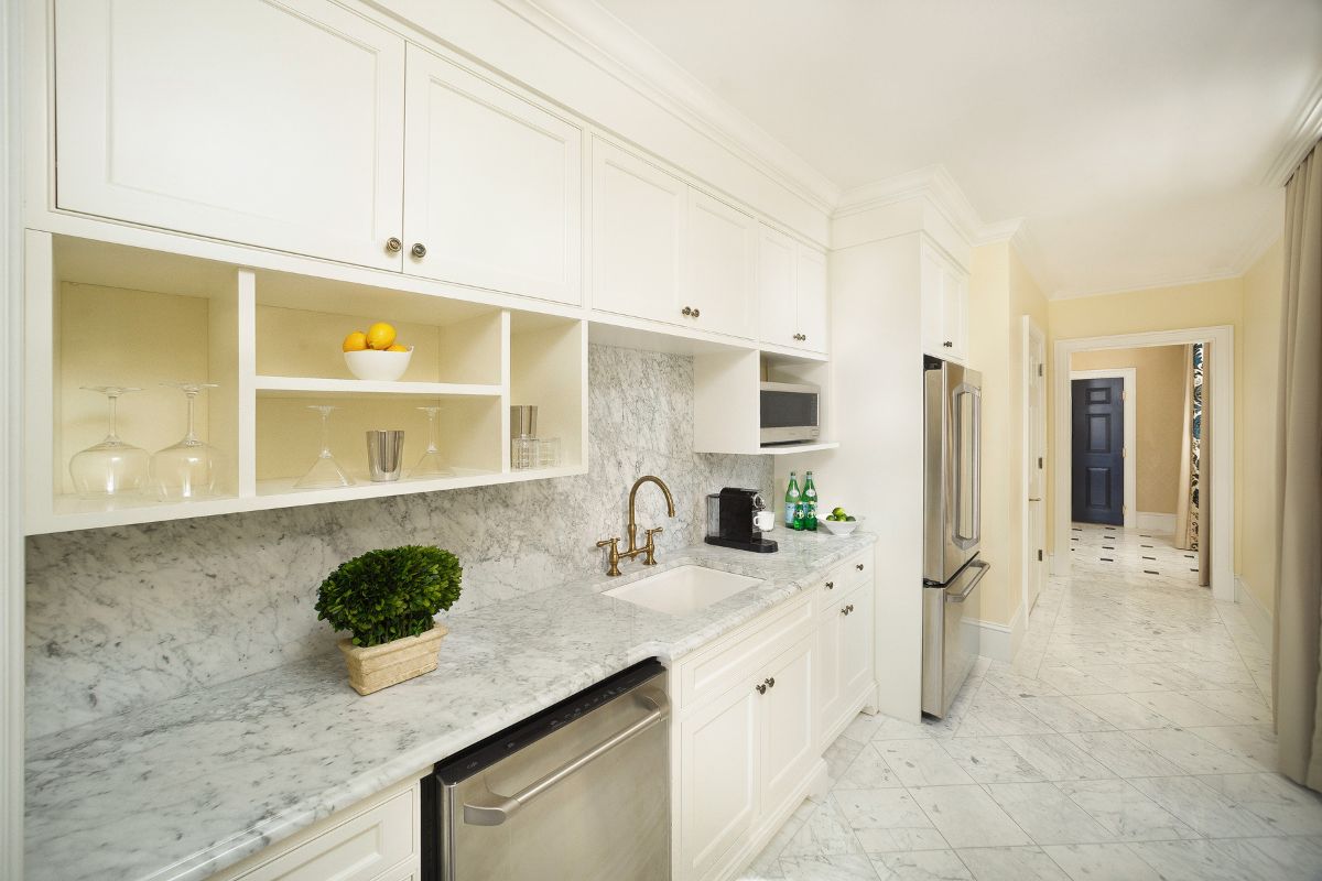 a kitchen with white cabinets and marble counter tops