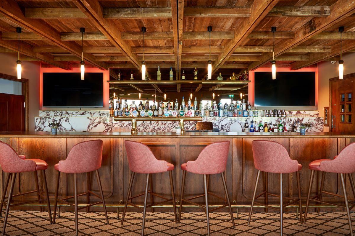 a bar with pink chairs and a counter with a bar and tvs