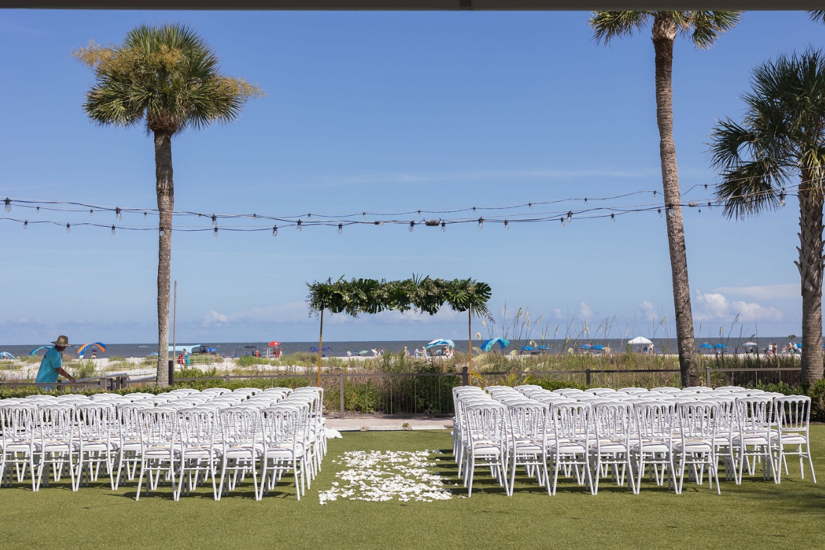 a group of chairs in a field with palm trees and a beach in the background
