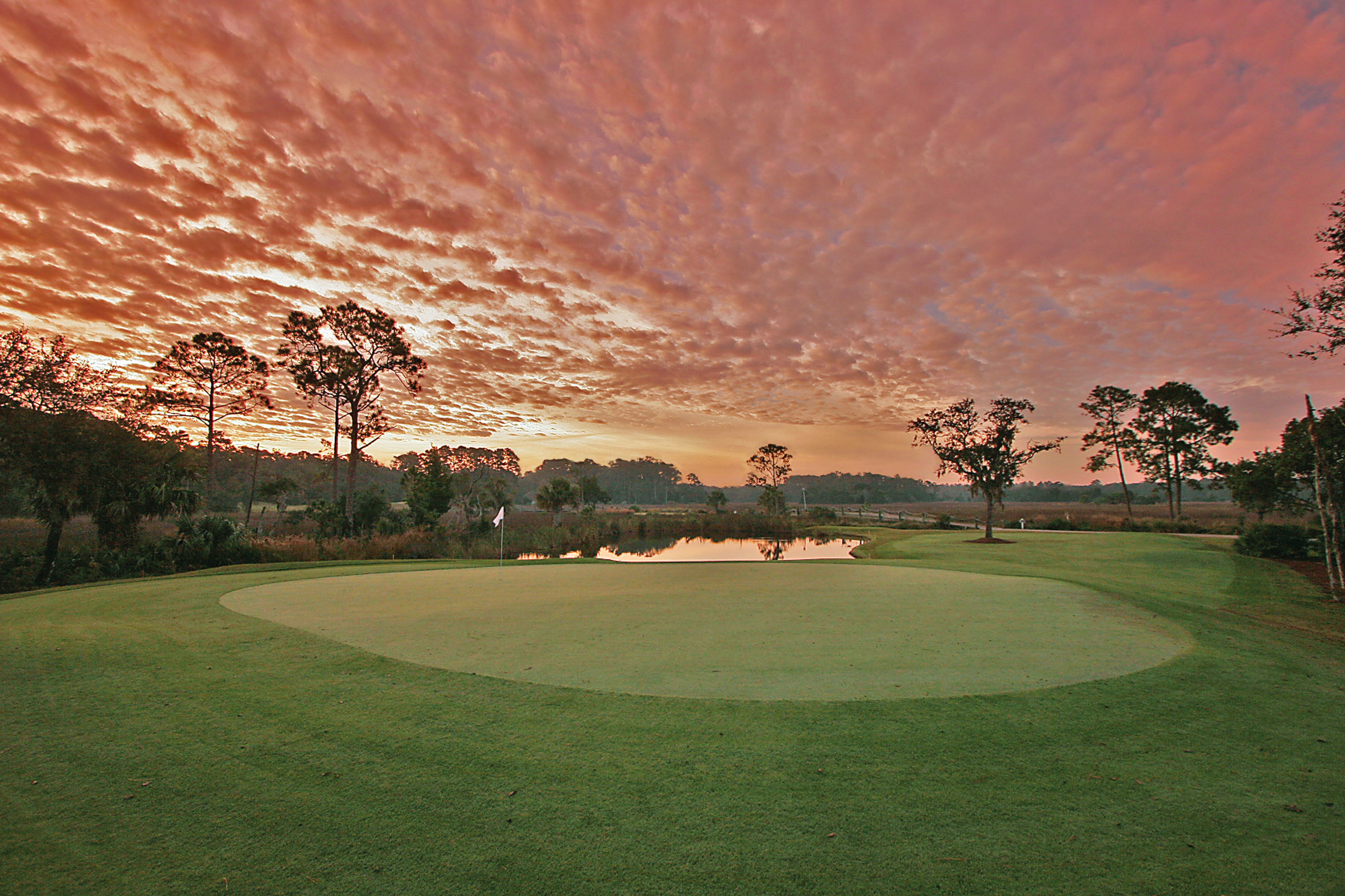a golf course with a hole in the middle and a pink sky with clouds