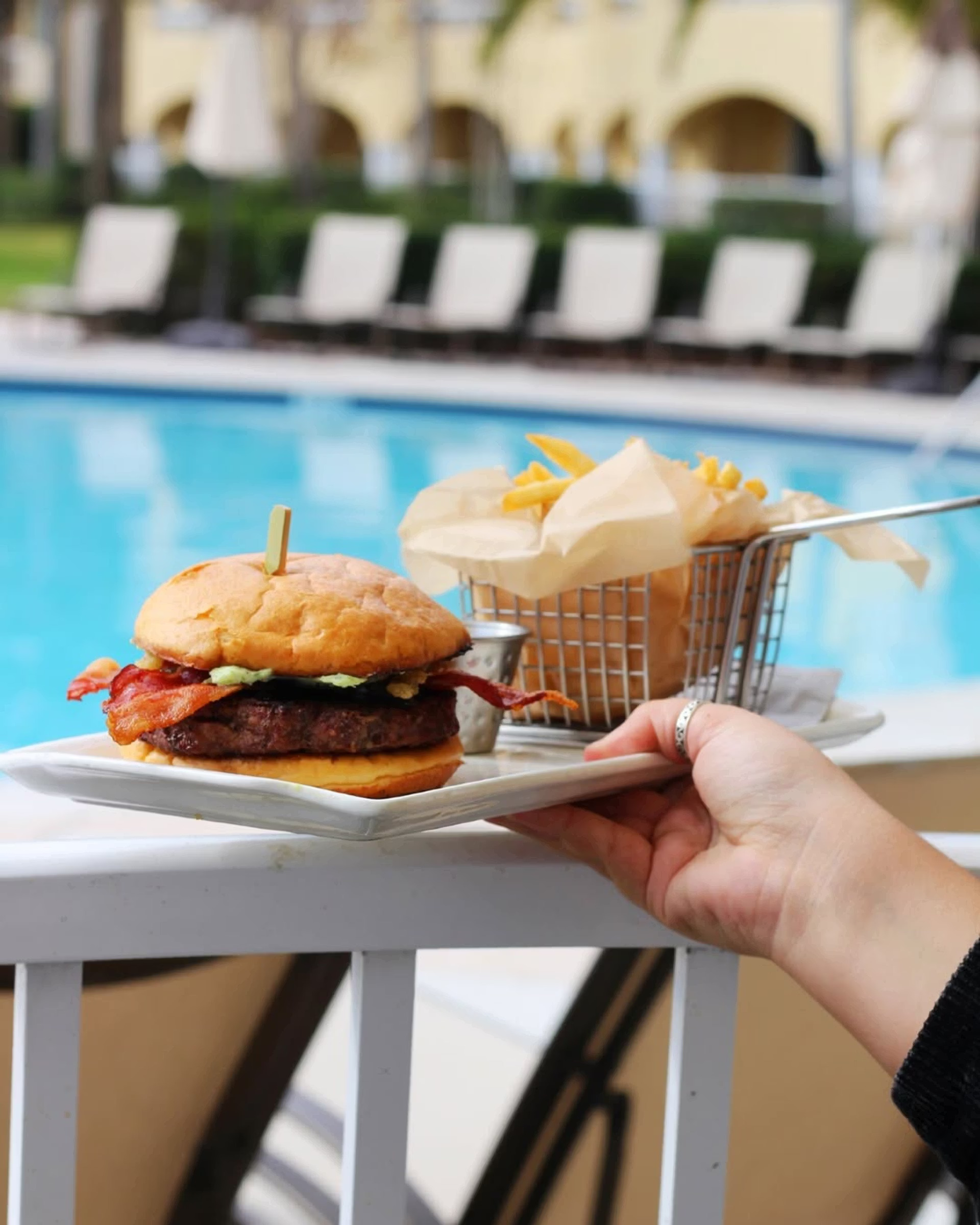 a hand holding a plate of burger and fries