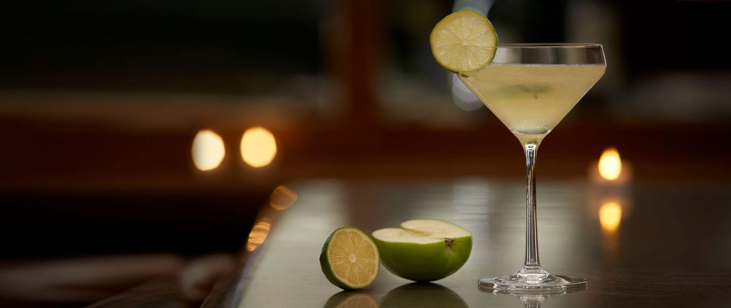 a glass with a drink and limes on a table