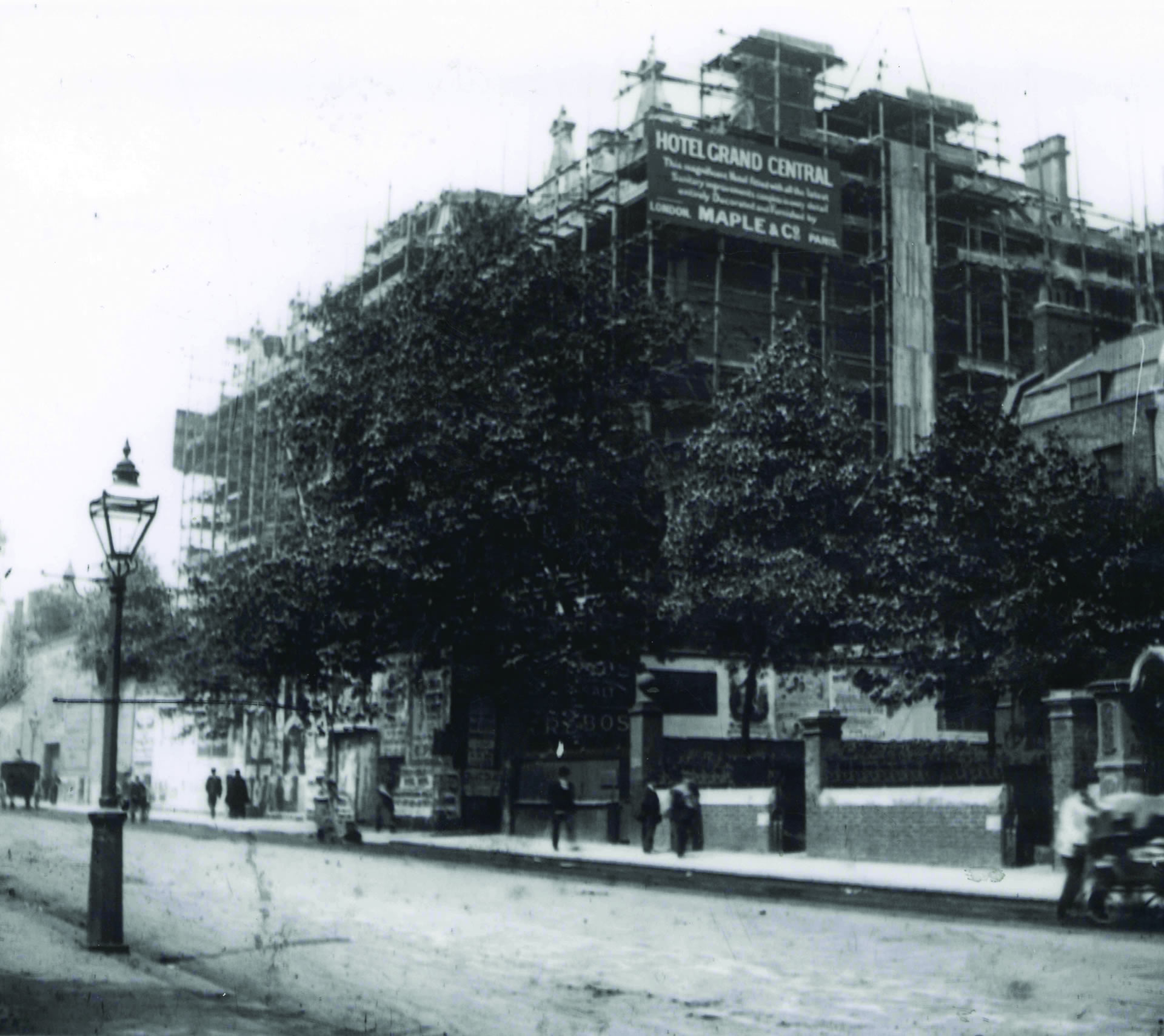 a building under construction with trees and people walking on the street