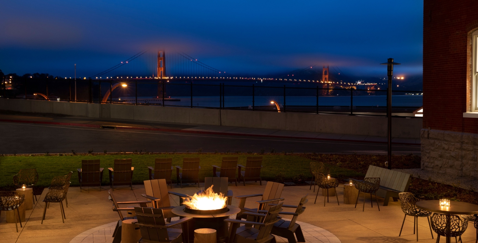 a fire pit with chairs around it and a bridge in the background